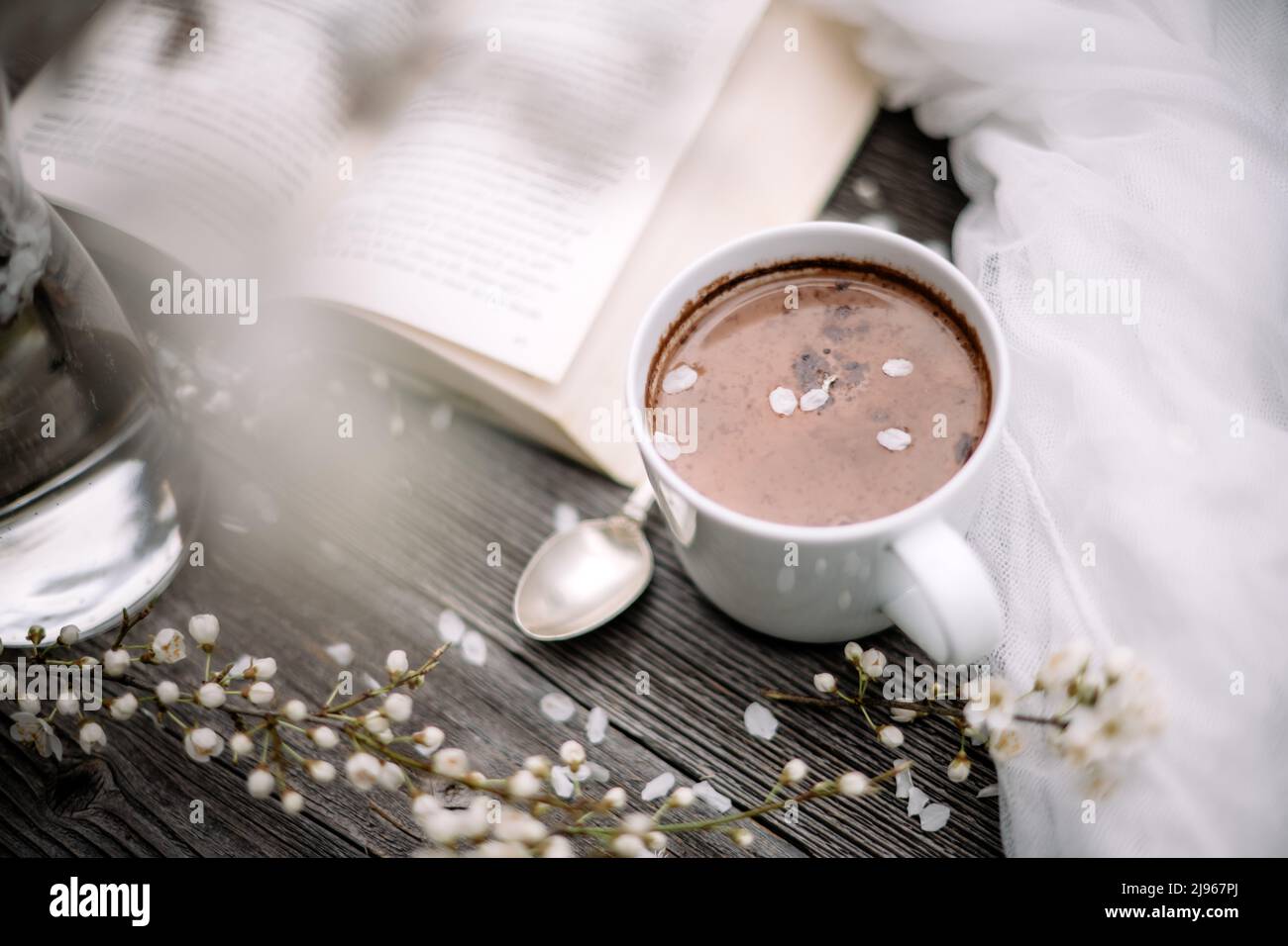 Tasse de cacao au chocolat chaud, vieux livre et fleurs de cerisier de printemps sur fond de bois. Concept de lecture Banque D'Images