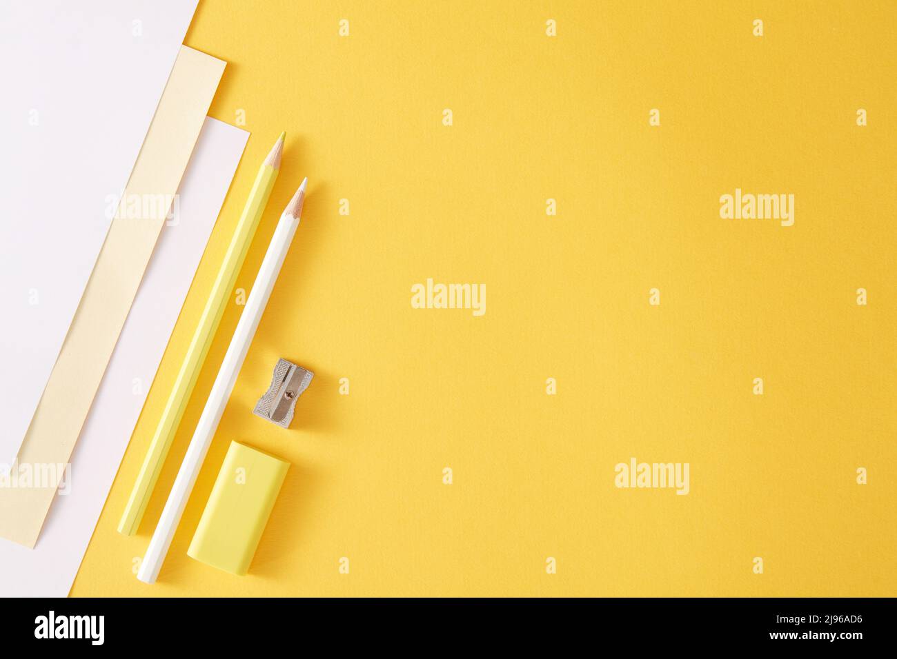 Crayons jaunes et blancs, livres blancs et taille-crayons en métal. Emplacement vide pour le texte ou le dessin sur fond jaune. Banque D'Images