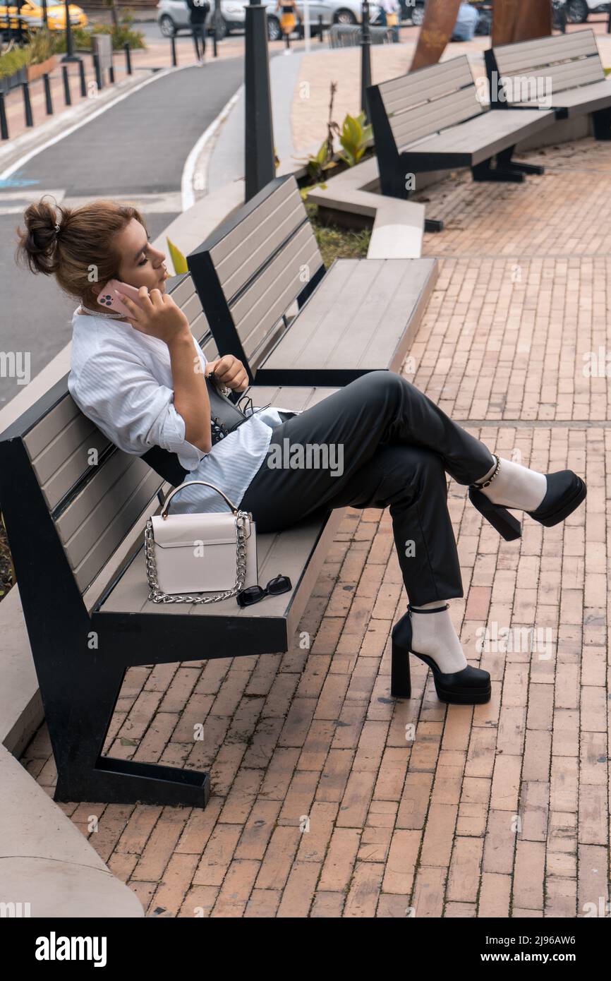 homme non binaire parlant en utilisant le téléphone dans ses mains penchées sur le banc de stationnement dans la rue Banque D'Images