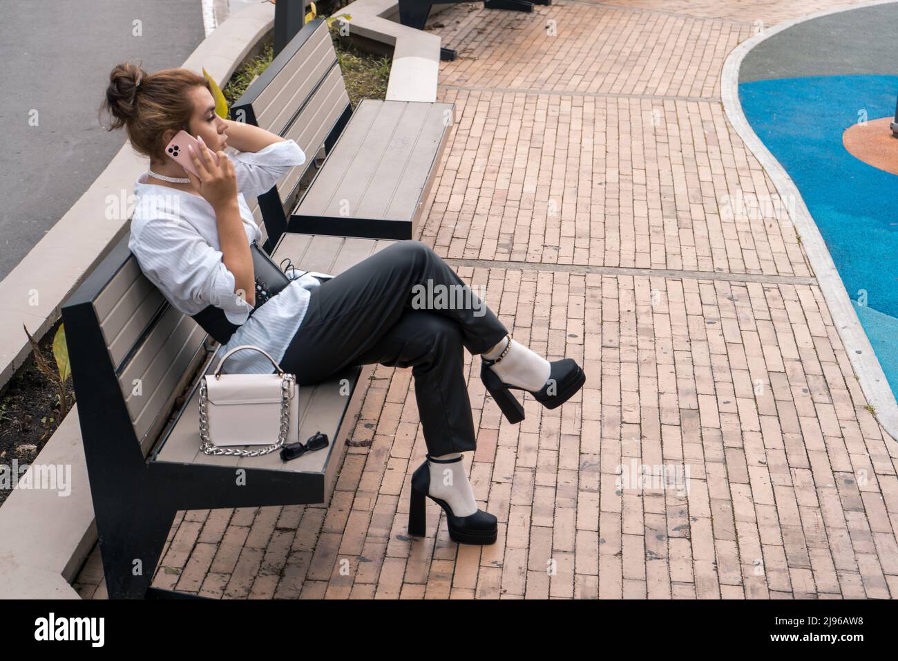 homme non binaire parlant en utilisant le téléphone dans ses mains penchées sur le banc de stationnement dans la rue Banque D'Images