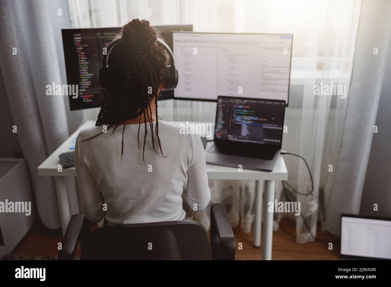 Arrière de la femme avec des tresses de boîte assis à la table codant sur l'ordinateur portable regardant le moniteur de compter Banque D'Images