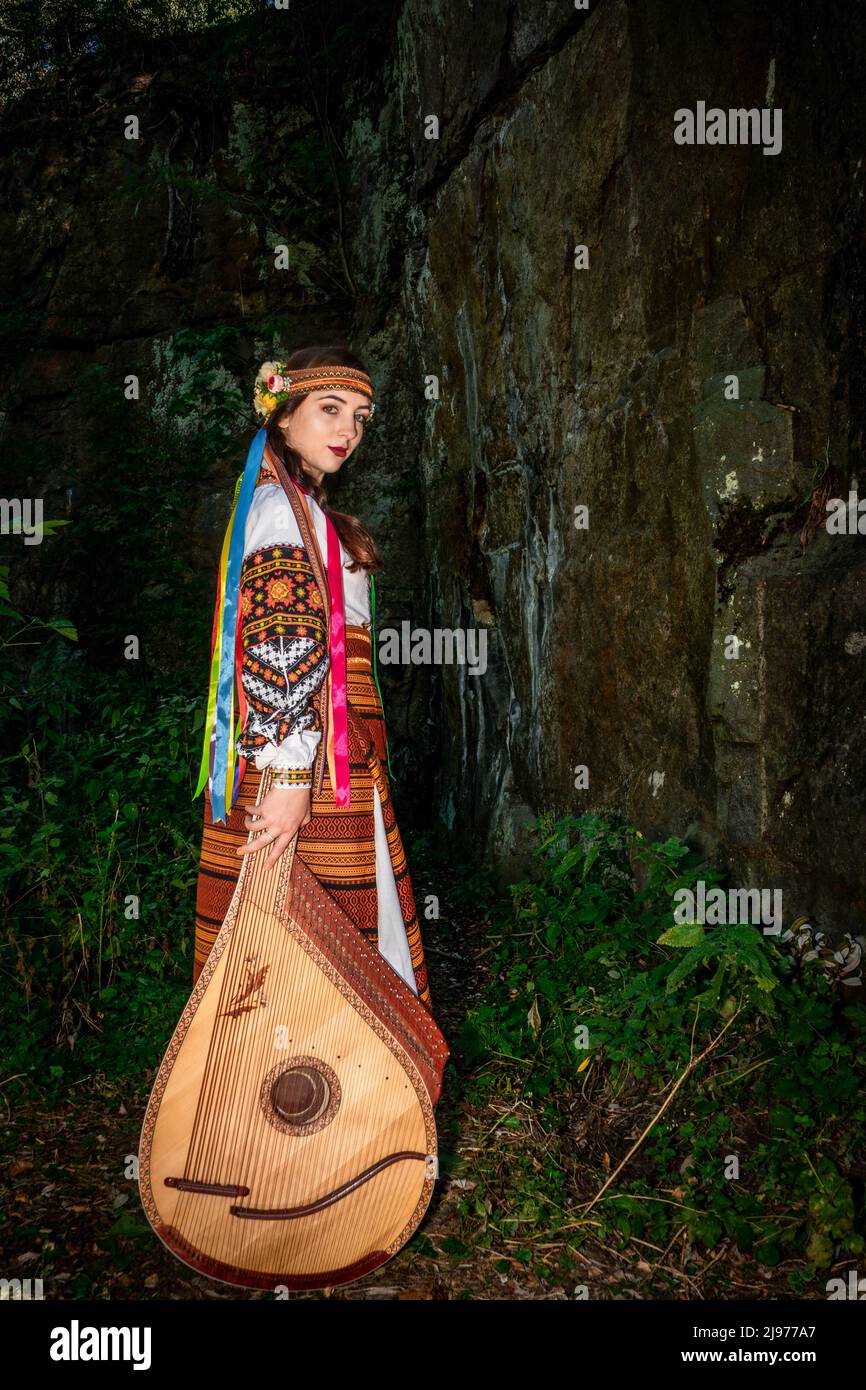 Femme ukrainienne en robe nationale avec un instrument de musique bandura tient près d'un rocher. Banque D'Images