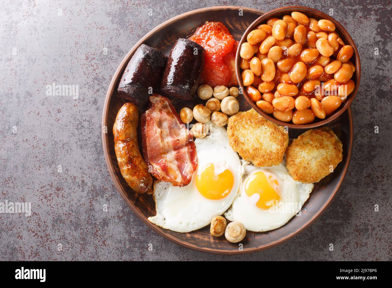 Petit déjeuner irlandais complet, pouding noir, œufs, haricots, saucisses, bacon, hachez le brun, le gros plan de la tomate dans l'assiette de la table. Vue horizontale du dessus Banque D'Images