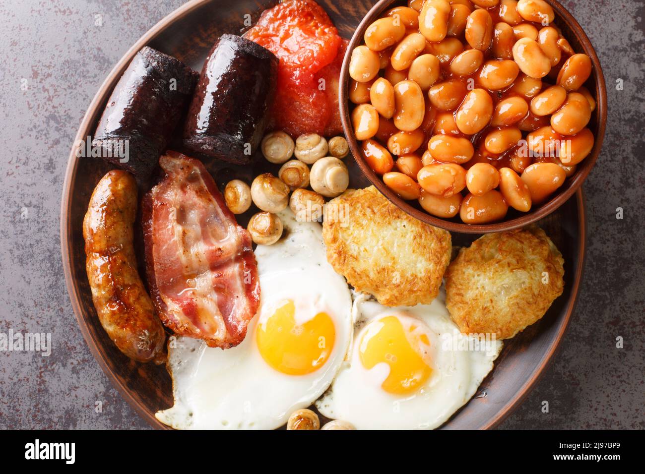 Petit déjeuner anglais complet avec œufs frits, saucisses, bacon, pudding noir, haricots, gros plan de tomates dans la plaque de la table. Vue de dessus horizontale fr Banque D'Images