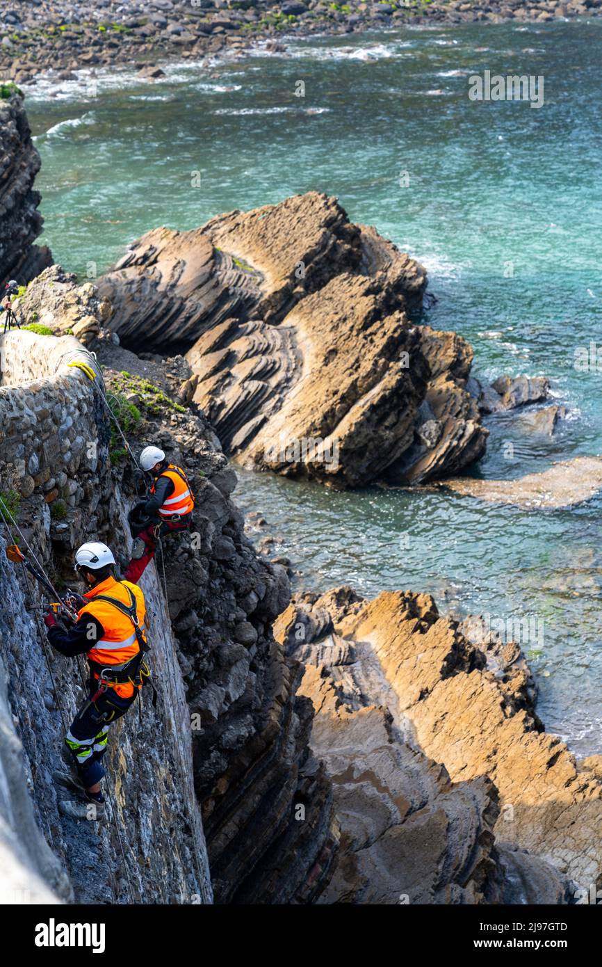 Bakio, Espagne - 3 mai 2022 : des techniciens d'accès à la corde et des ouvriers de la construction réparent les murs et le pont en pierre historiques sur la côte basque espagnole Banque D'Images
