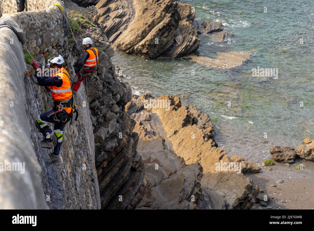 Bakio, Espagne - 3 mai 2022 : des techniciens d'accès à la corde et des ouvriers de la construction réparent les murs et le pont en pierre historiques sur la côte basque espagnole Banque D'Images