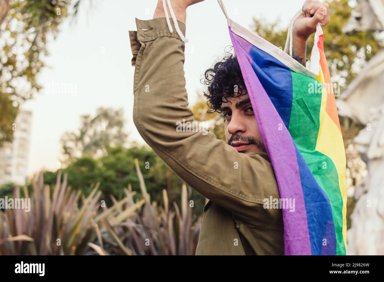 vue arrière de l'homme caucasien à l'extérieur, portant le drapeau de fierté gay, regardant la caméra. Banque D'Images