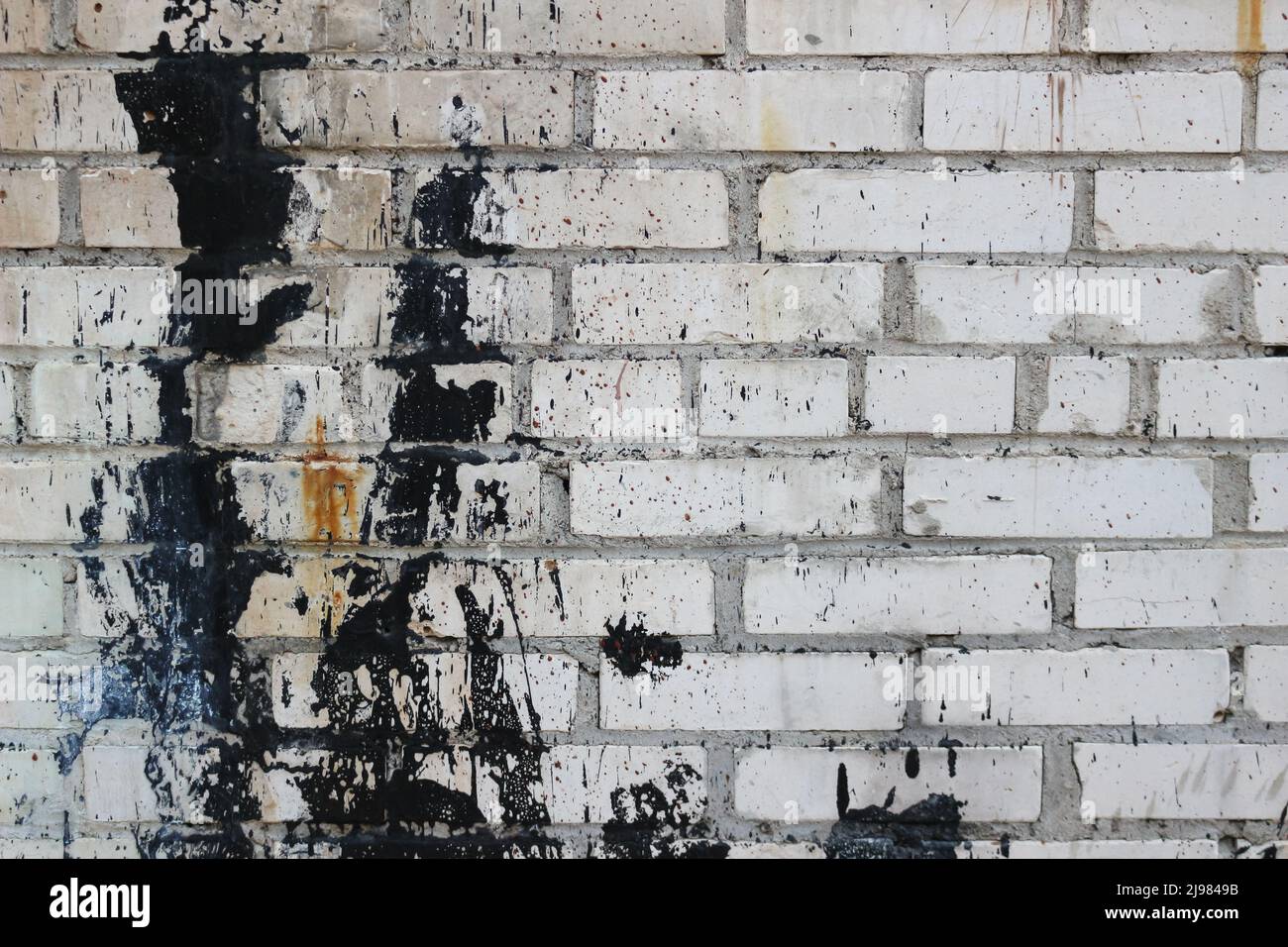 Vieux mur de briques avec des éclaboussures de peinture noire. Banque D'Images