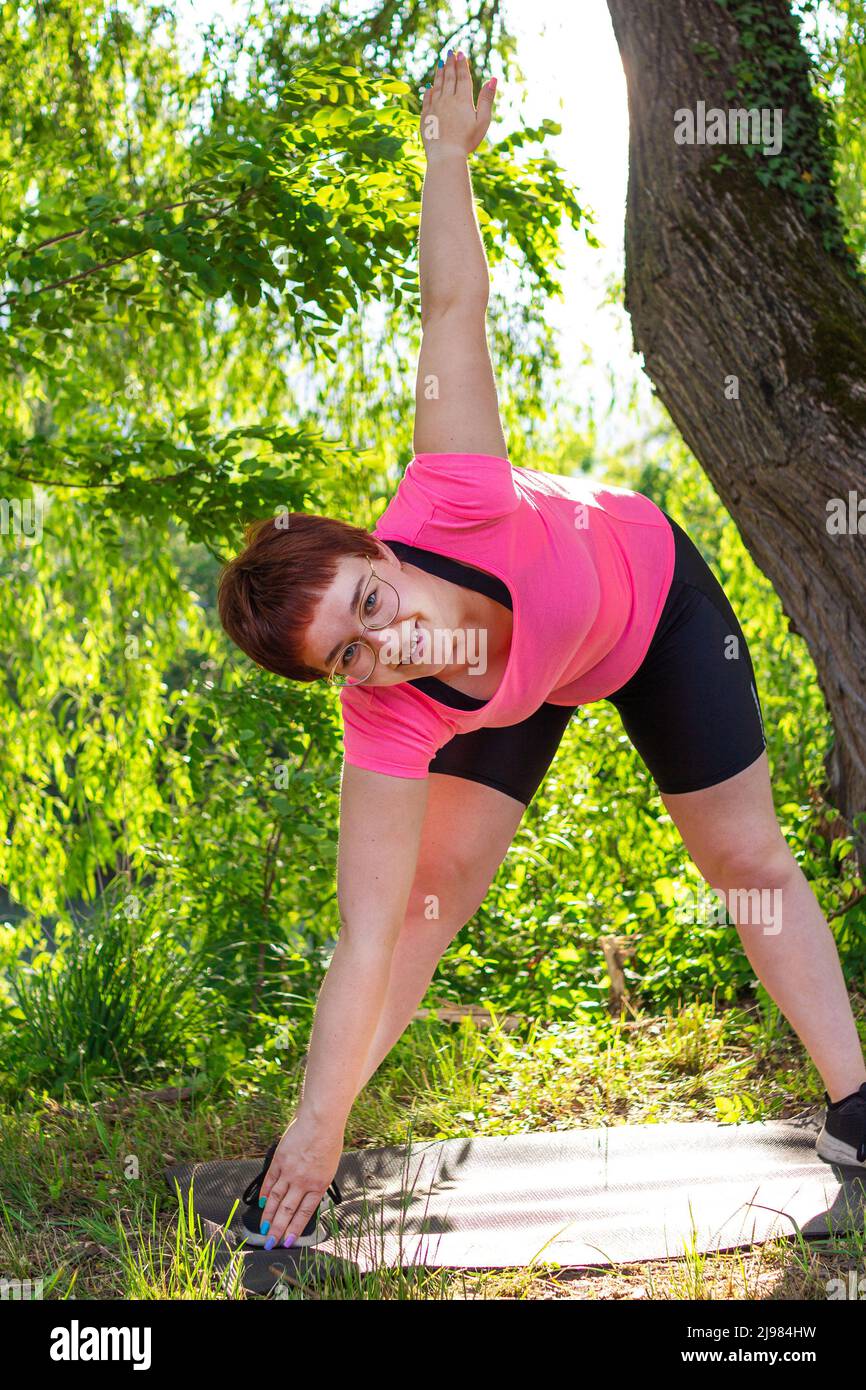 Belle jeune femme essayant de se mettre en forme pour l'été; l'activité d'ion un tapis de yoga dans un parc Banque D'Images