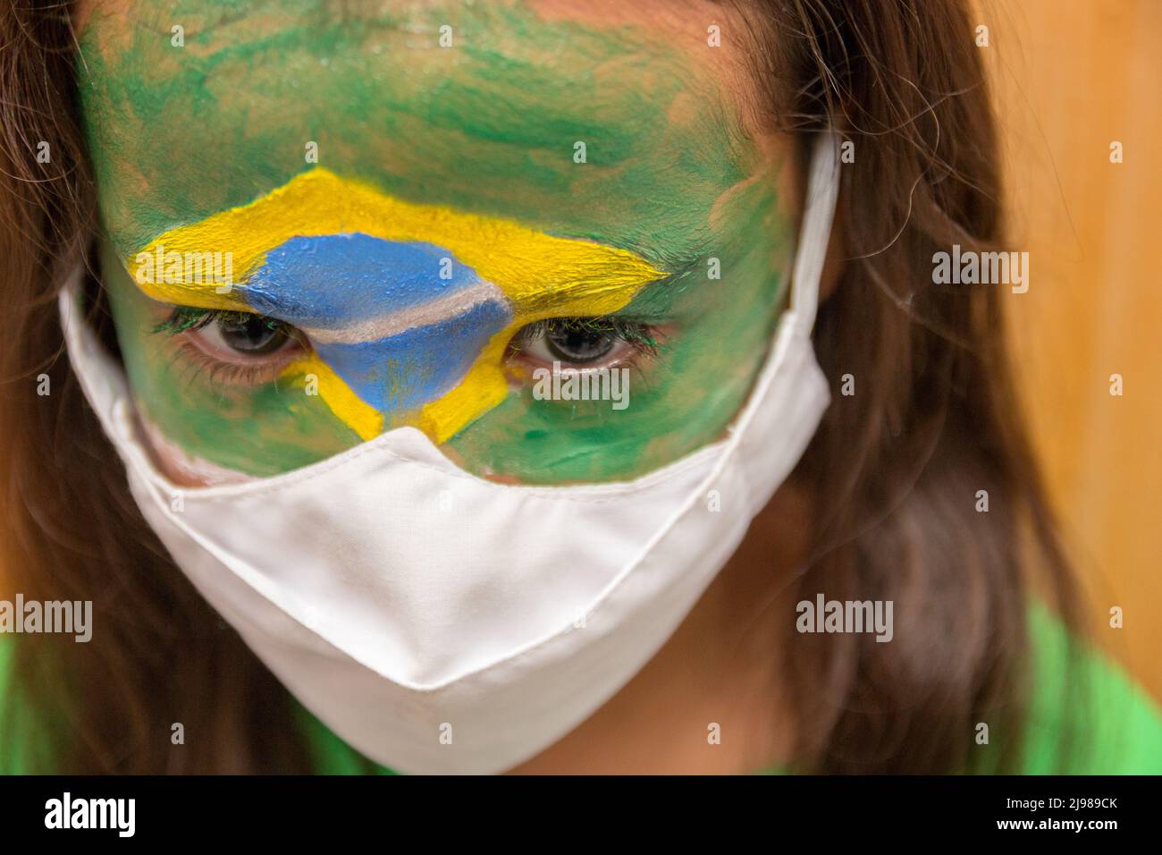 Enfant avec un masque avec son visage peint avec le drapeau du Brésil. Banque D'Images