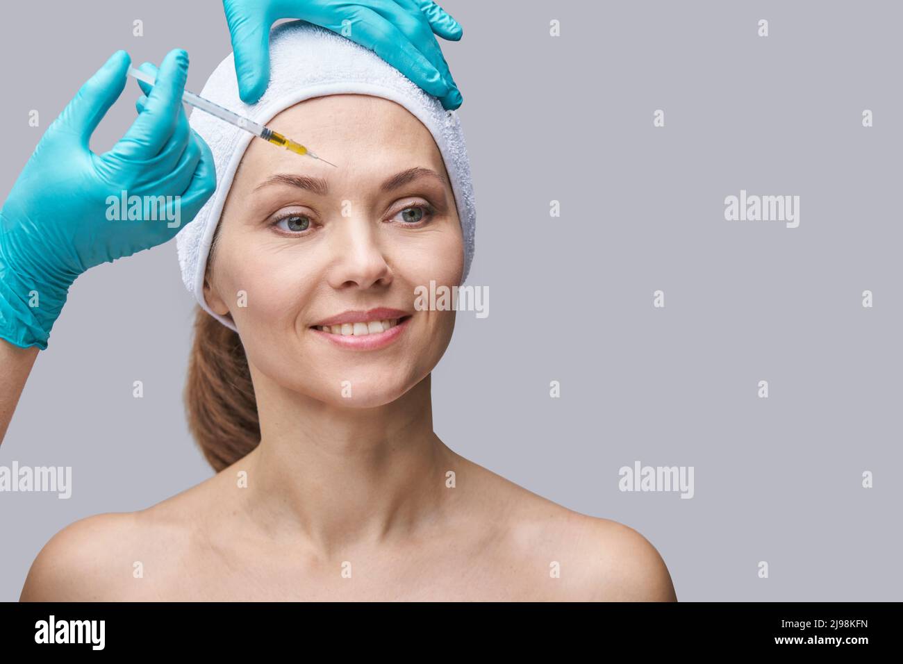 Injection de l'aiguille de face. Jeune femme procédure de cosmétologie. Main médecin dans un gant vert. Jolie patiente. Salon de spa front. Soins de beauté. Peau saine. Rajeunissement par plasmolisation. Dermatologie Banque D'Images