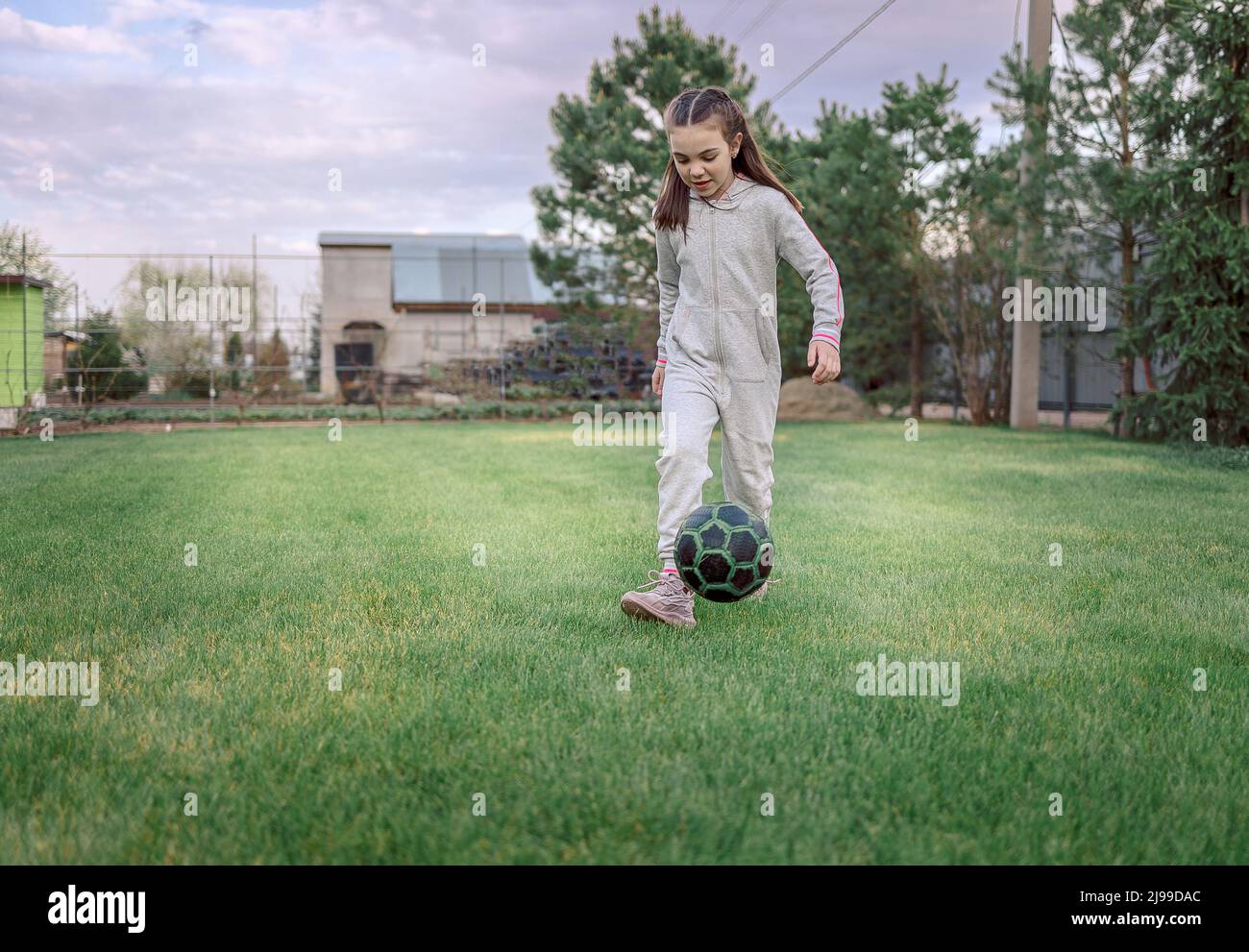 Jolie petite fille jouant au football avec ballon de football sur pelouse verte dans l'arrière-cour de la maison. Un enfant donne un coup de pied au ballon de football sur le terrain. Photo de haute qualité Banque D'Images