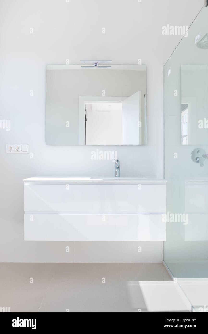 Partie d'une salle de bains moderne. Vue sur une armoire blanche avec un lavabo et une cabine de douche en verre. Banque D'Images