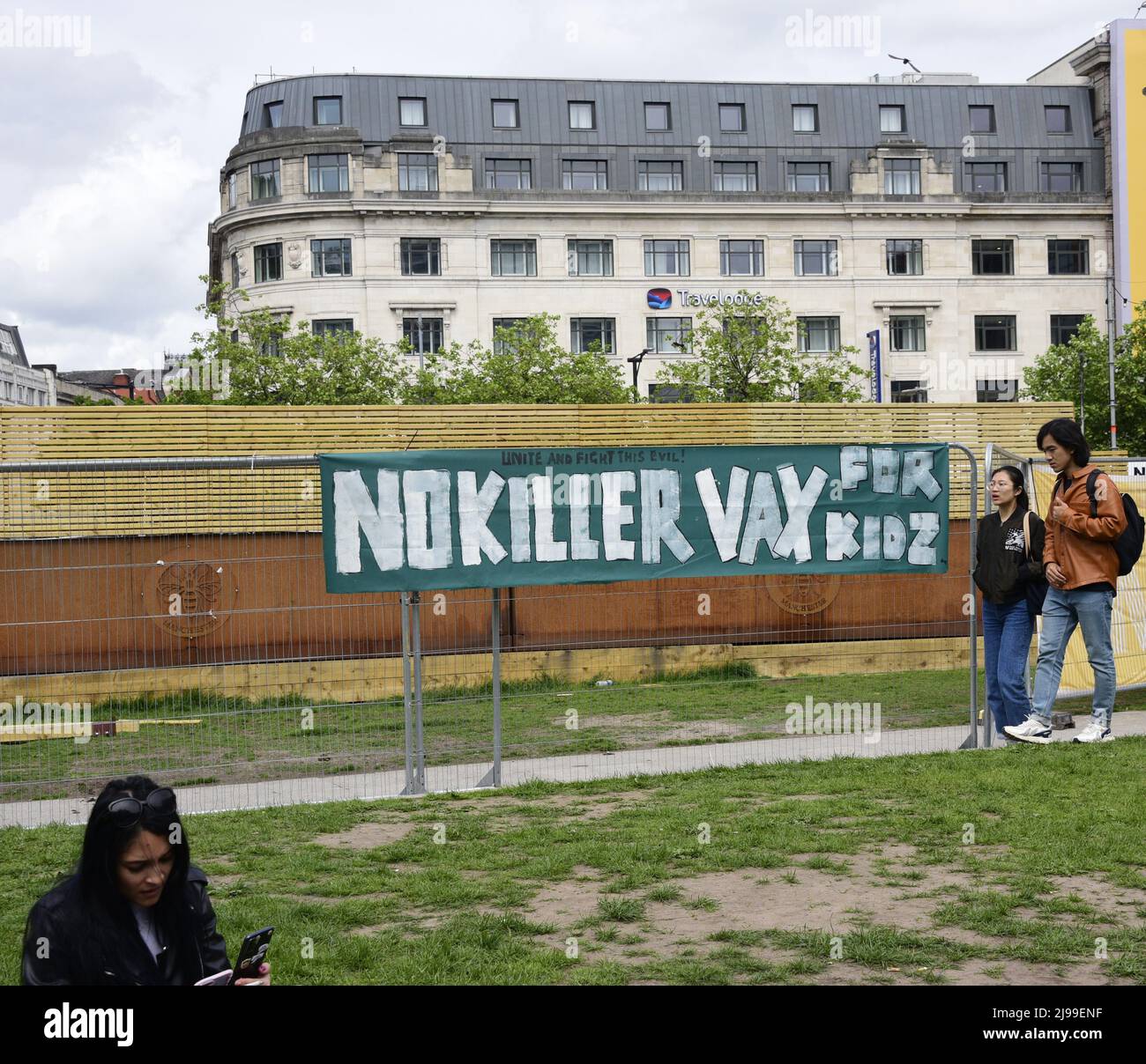 Les gens marchent au-delà d'une bannière lisant "No killer vax for kidz" sur une clôture dans le centre de Manchester, Angleterre, Royaume-Uni, Iles britanniques. La vie quotidienne à Manchester, Royaume-Uni. Banque D'Images