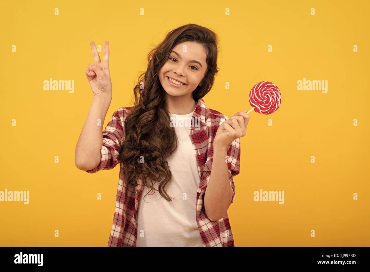 drôle enfant tenir lollipop caramel bonbon sur fond jaune montrer le geste de paix, l'enfance. Banque D'Images
