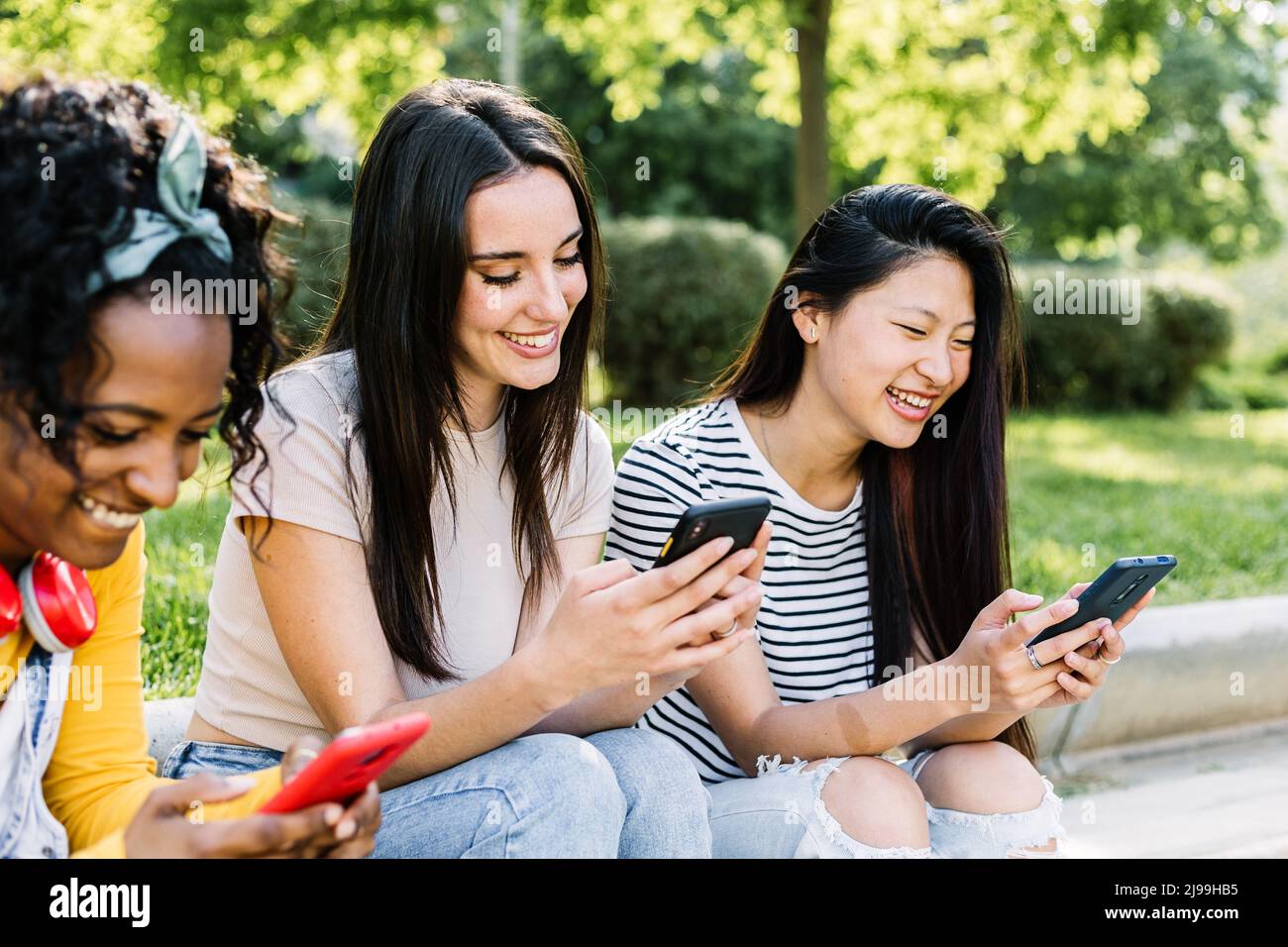 Trois jeunes amies multiraciales qui utilisent un téléphone portable ensemble en extérieur Banque D'Images