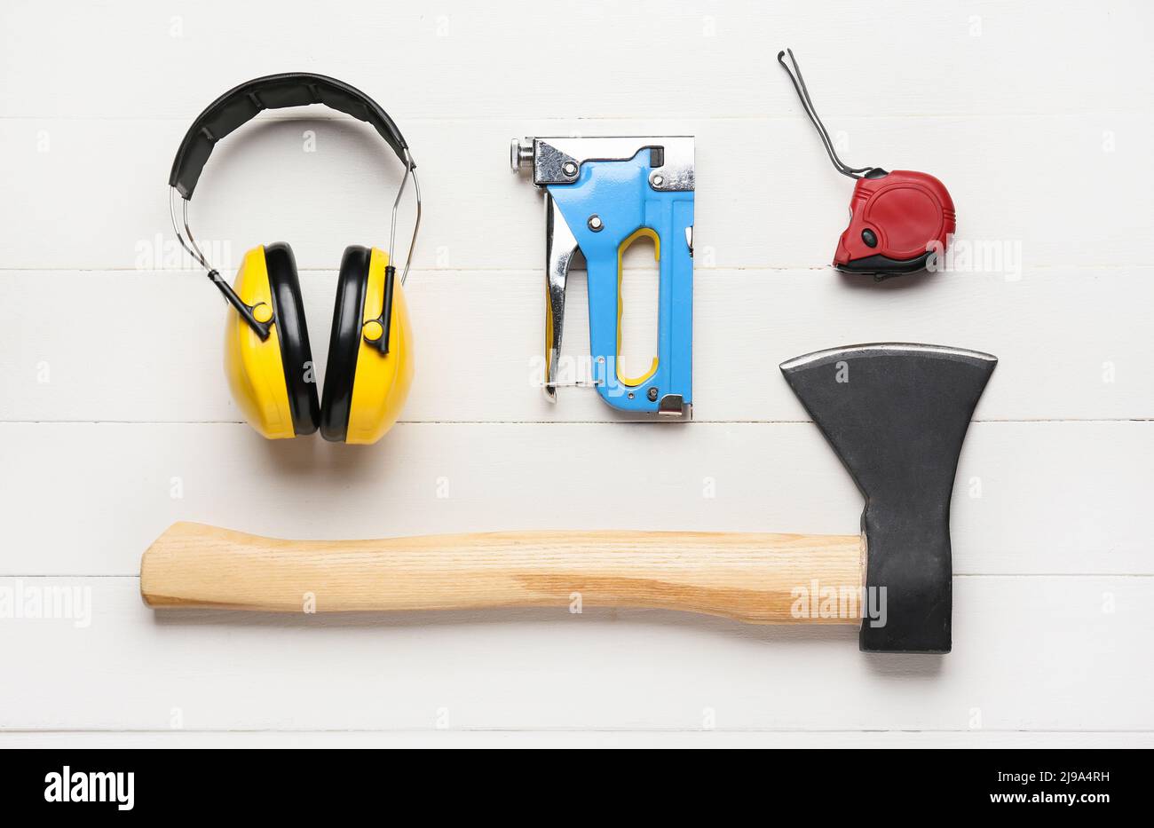 Casque de protection jaune, agrafeuse, règle et hache sur fond blanc en bois Banque D'Images