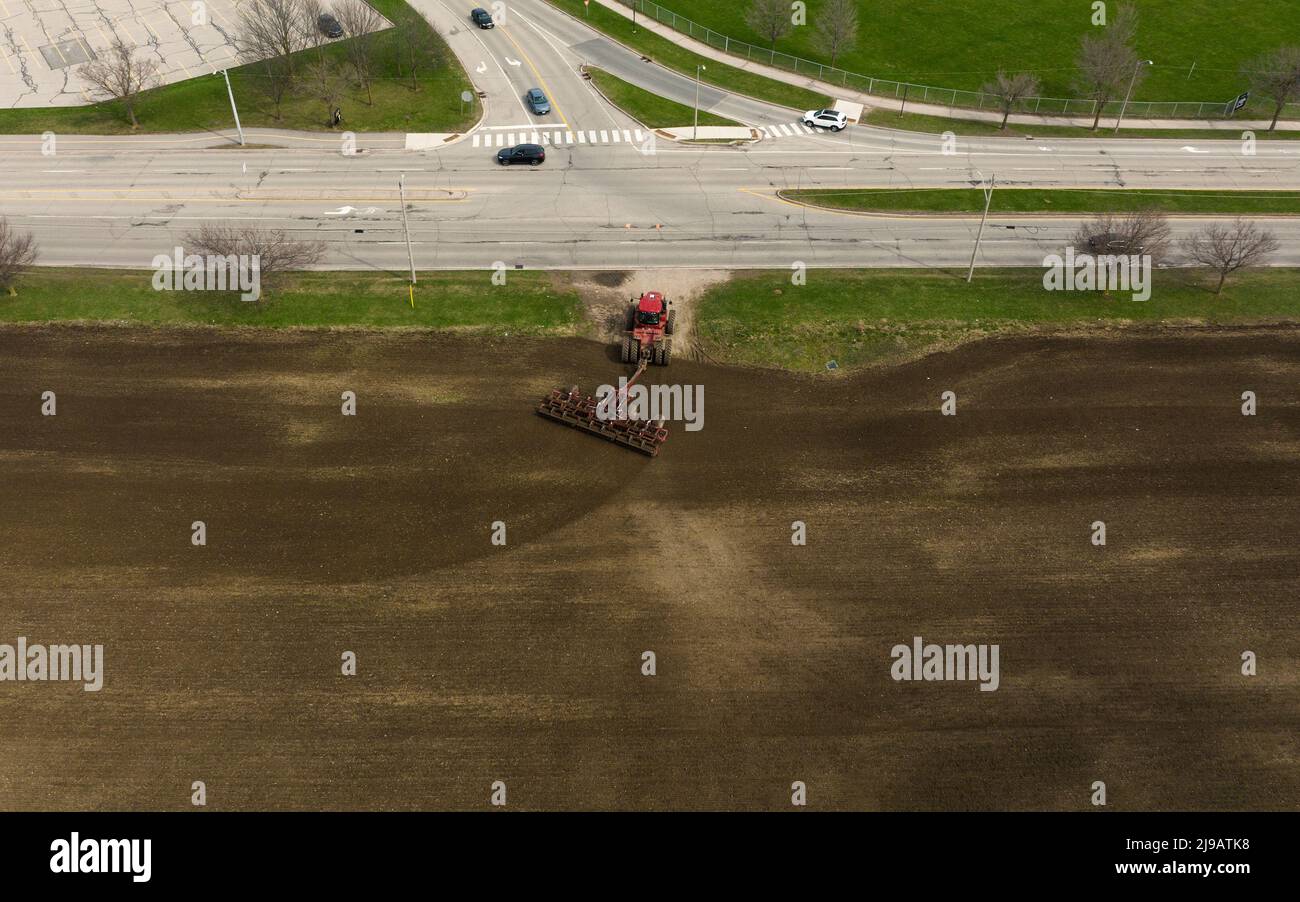 Une vue aérienne au-dessus d'un champ, comme un grand tracteur rouge, est vue en quittant un champ au début de la saison agricole. Banque D'Images