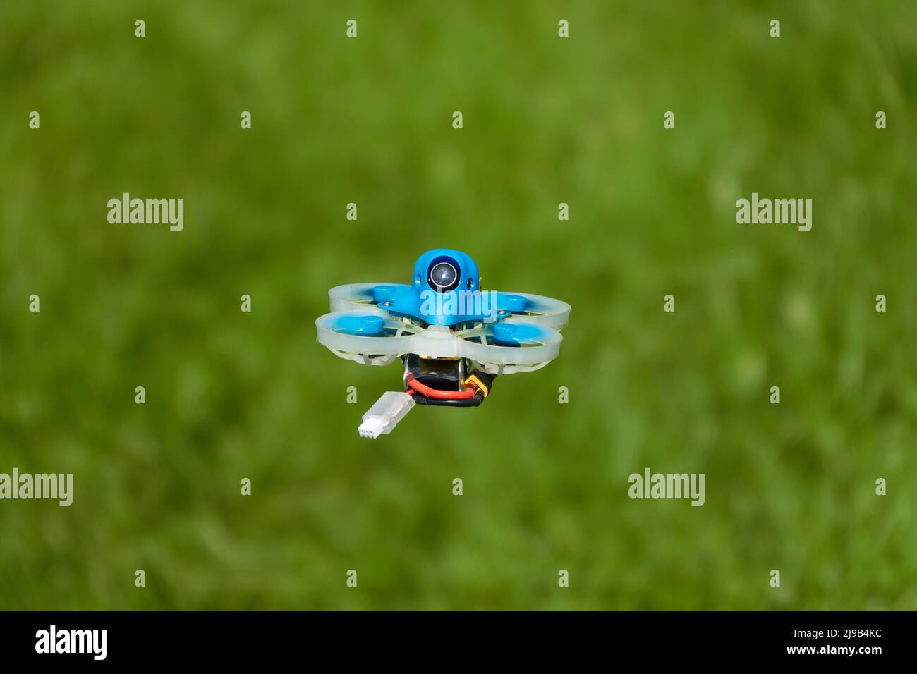 Petit bleu Drone également quad de course, avec la gondole de protection en blanc avec un fond flou de vert.Allemagne. Banque D'Images