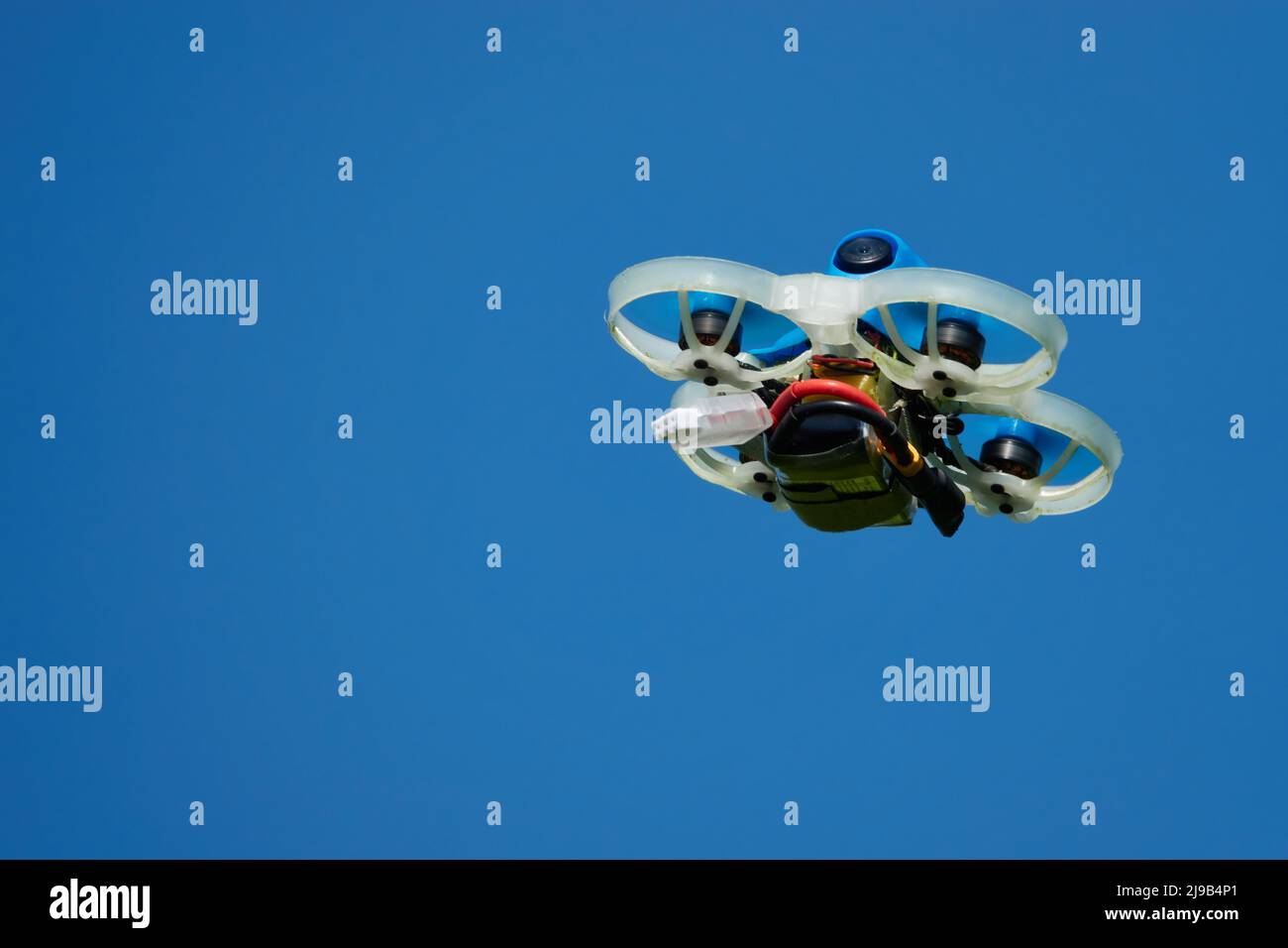 Petit Drone bleu également quad de course, avec la gondole de protection en blanc avec un ciel bleu. Photographié de dessous.Allemagne. Banque D'Images
