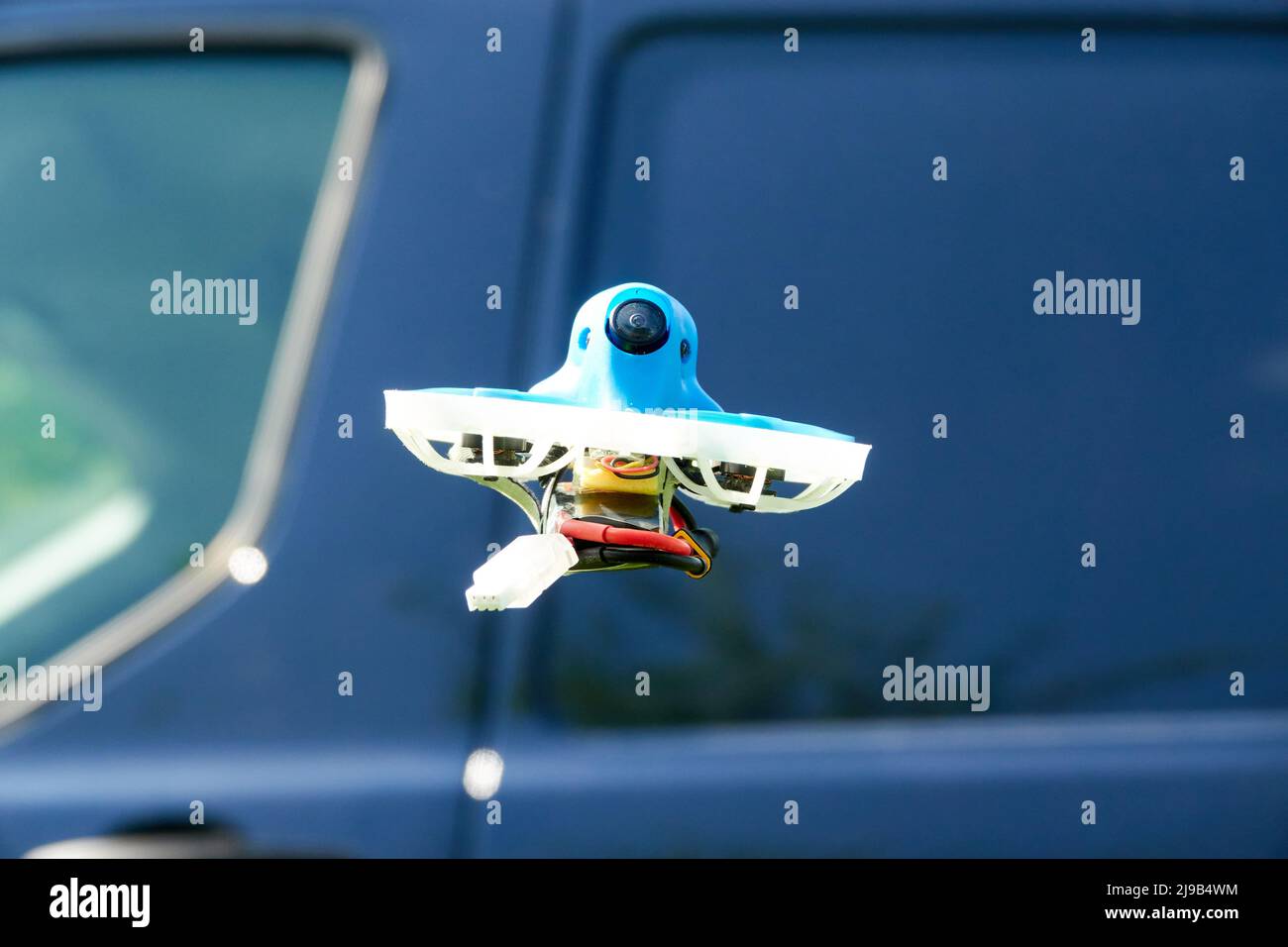 Petit bleu Drone également quad de course, avec la gondole de protection en blanc avec un ciel bleu, une voiture bleue en arrière-plan. Photographié d'en dessous. Allemagne. Banque D'Images