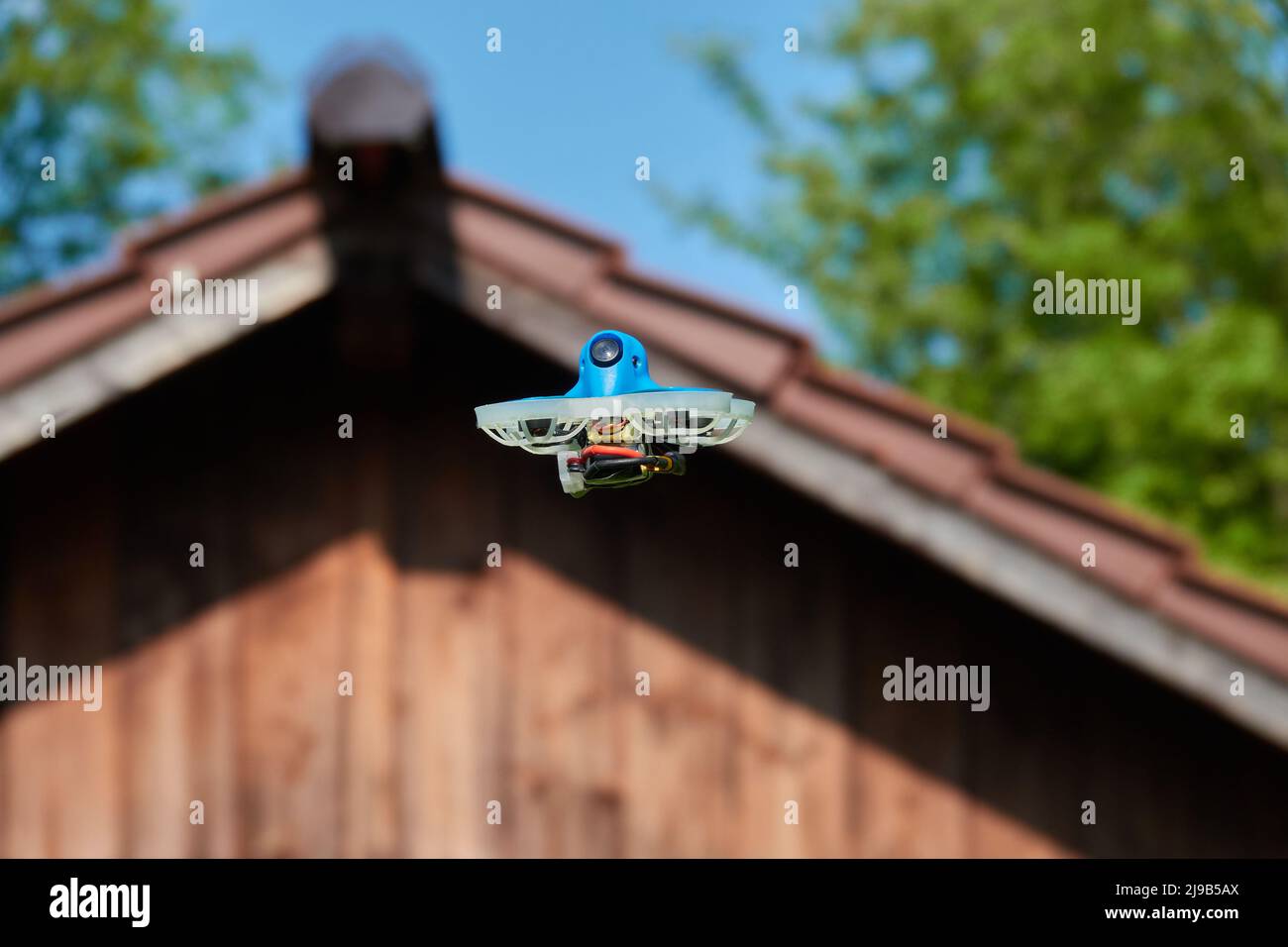 Petit drone également la course quad en bleu, voler sur le toit d'une hutte en marron. Arbres et ciel bleu en arrière-plan. Allemagne. Banque D'Images