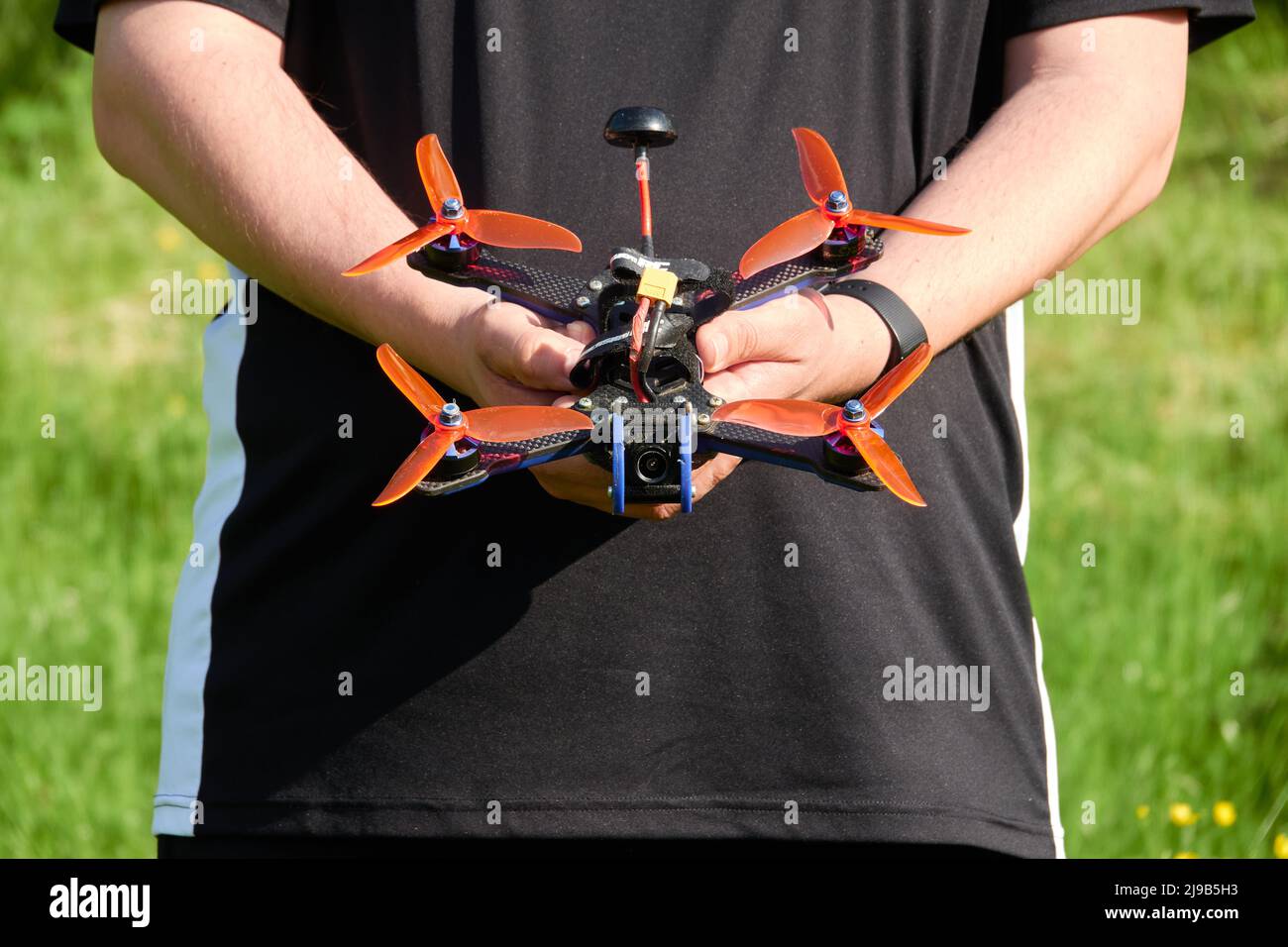 Le drone noir également quad de course, avec hélice orange, est tenu par les mains humaines. Herbe floue en arrière-plan. Allemagne. Banque D'Images