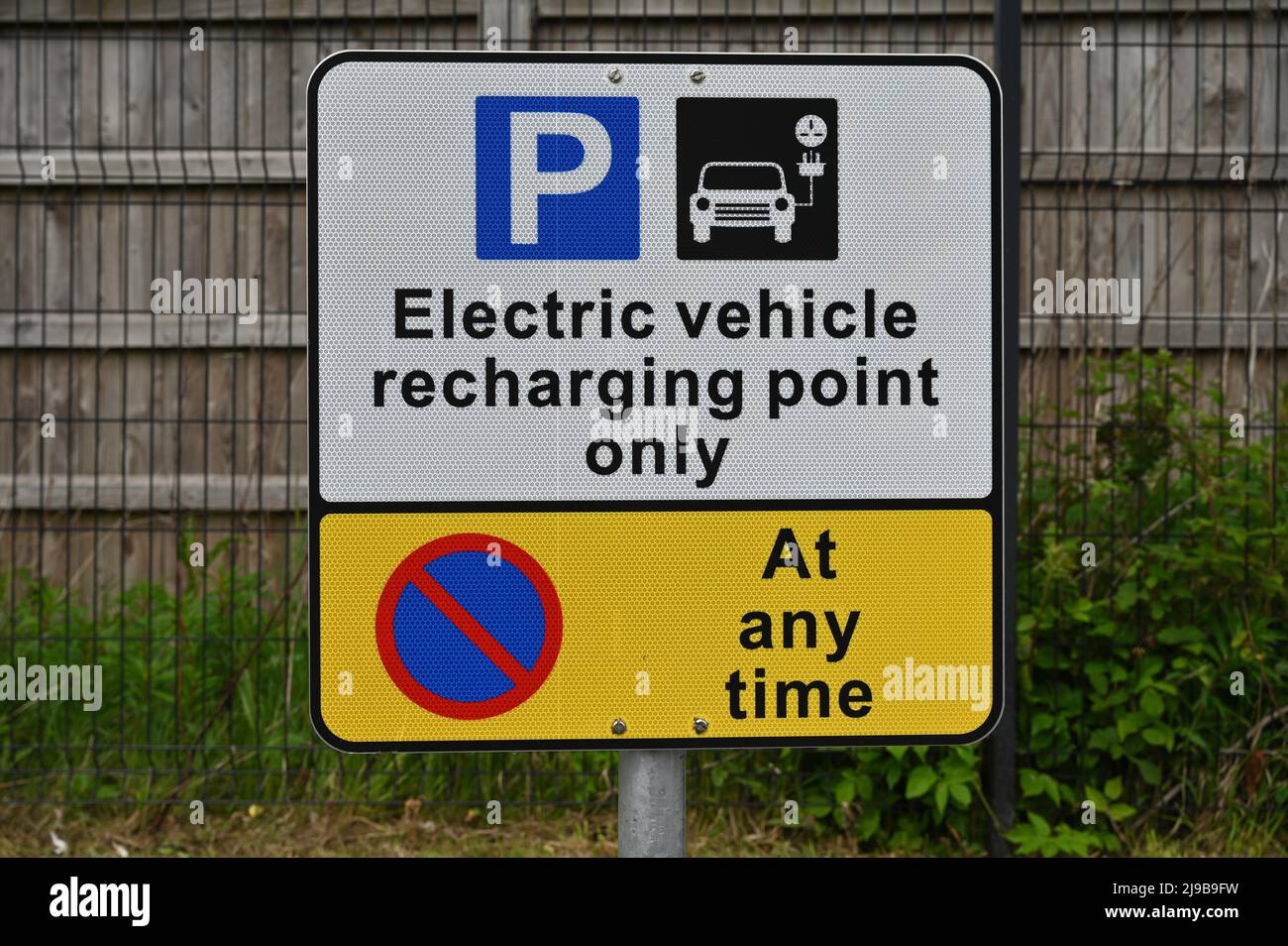 Panneau de point de recharge de véhicule électrique UK, isolé contre l'herbe et le fond de clôture en bois Banque D'Images