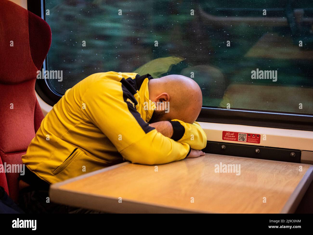 Un homme complètement chauve portant un haut jaune vif est vu endormi sur une table dans un train près de Leeds en Angleterre. Banque D'Images