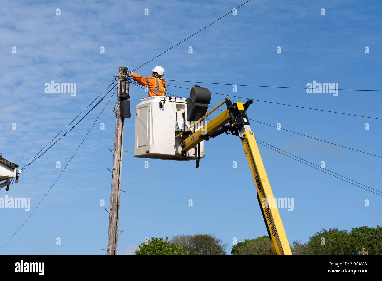 Un technicien de réparation Openreach portant un EPI dans un préparateur de cerisier réparant les câbles téléphoniques aériens sur un poteau téléphonique BT en bois au pays de Galles, au Royaume-Uni Banque D'Images