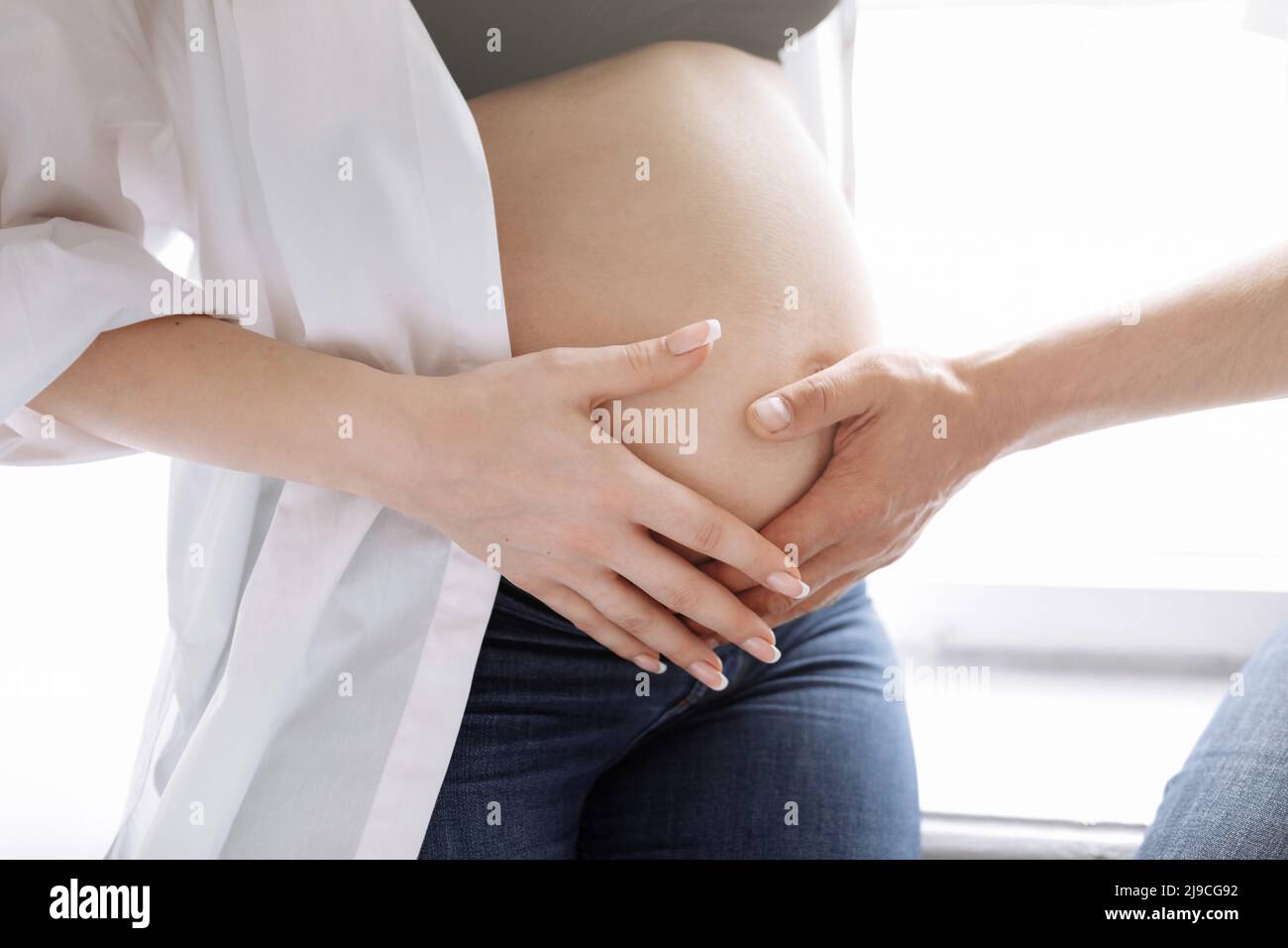 Photo rognée d'un couple enceinte à la maison, l'homme est embrassant et touchant la femme grand ventre. Grossesse, parentalité, amour, concept de famille. Photo de haute qualité. Banque D'Images