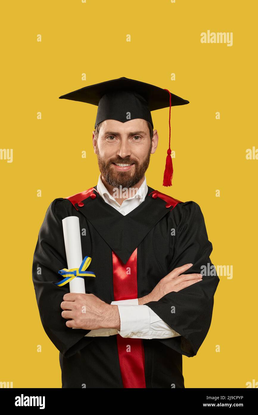 Vue avant de l'homme avec la barbe diplômé de l'université, université. Diplômé portant un mortier debout avec des mains croisées, souriant, titulaire d'un diplôme. Concept de l'école secondaire. Banque D'Images Vue avant de l'homme avec la barbe diplômé de l'université, université. Diplômé portant un mortier debout avec des mains croisées, souriant, titulaire d'un diplôme. Concept de l'école secondaire. Banque D'Images