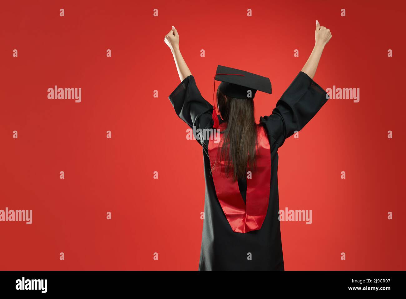 Vue arrière de la petite fille debout, diplômé de l'université, université. Brunette jeune femme avec de longs cheveux montrant un hurray, portant un mortaboard et une robe de troisième cycle. Concept de la jeunesse. Banque D'Images Vue arrière de la petite fille debout, diplômé de l'université, université. Brunette jeune femme avec de longs cheveux montrant un hurray, portant un mortaboard et une robe de troisième cycle. Concept de la jeunesse. Banque D'Images