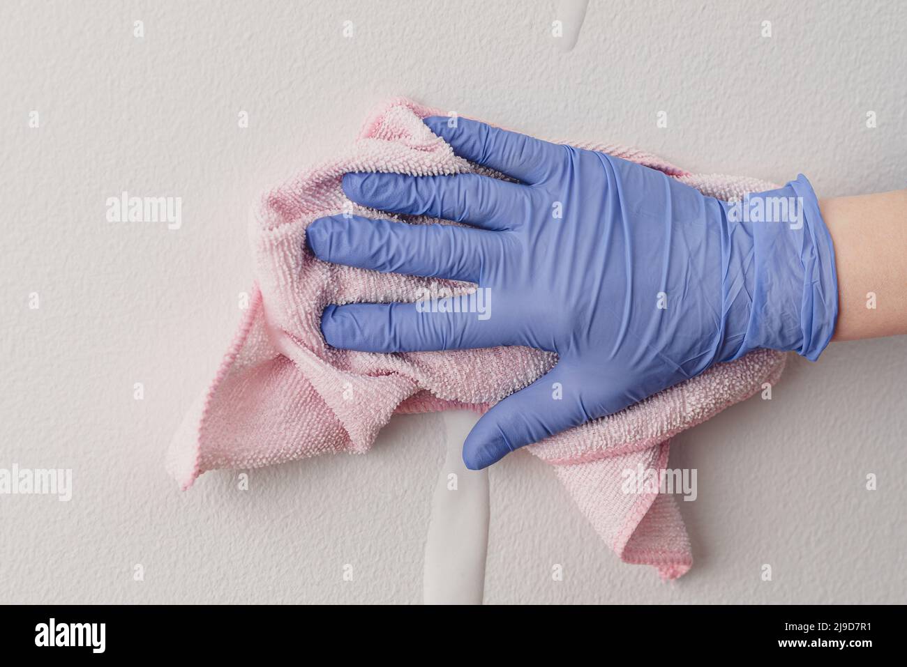 Main de l'employé dans un gant de protection en caoutchouc bleu avec un chiffon en microfibre essuyant la paroi de la poussière. La femme de ménage se soucie de la maison. Nettoyage commercial Banque D'Images