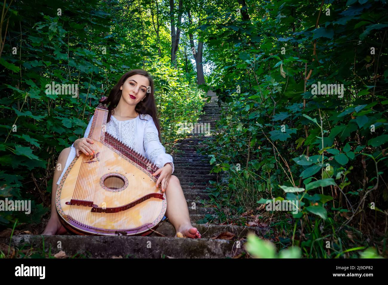 Une femme ukrainienne est assise sur les escaliers dans un vieux parc avec un instrument de musique bandura ukrainien. Banque D'Images