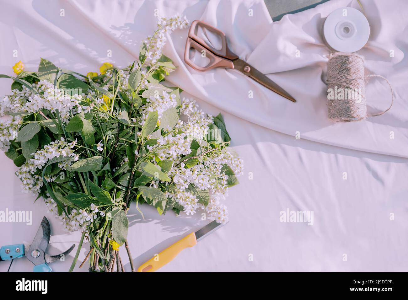 Le bureau de fleuriste avec des outils de travail sur fond clair et ensoleillé, des outils fleuristes comme des ciseaux, sécateurs, ficelle, couteau, fleurs Banque D'Images