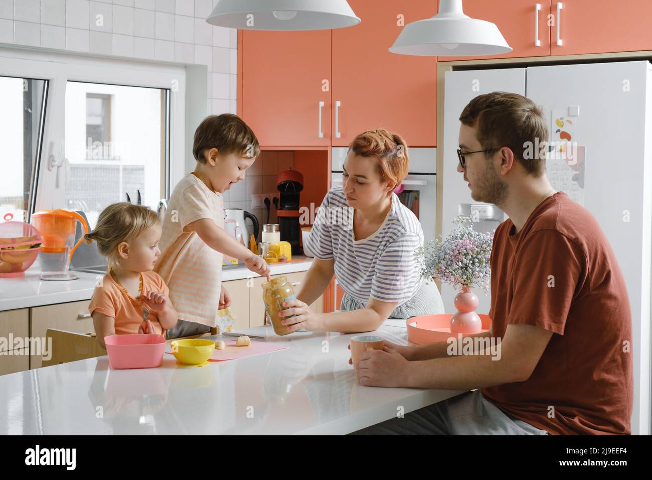 Une famille heureuse avec des enfants qui cuisent dans une cuisine moderne. Les enfants coupants de la salade de fruits, préparant des aliments avec leur mère et leur père. Une alimentation saine à la maison Banque D'Images