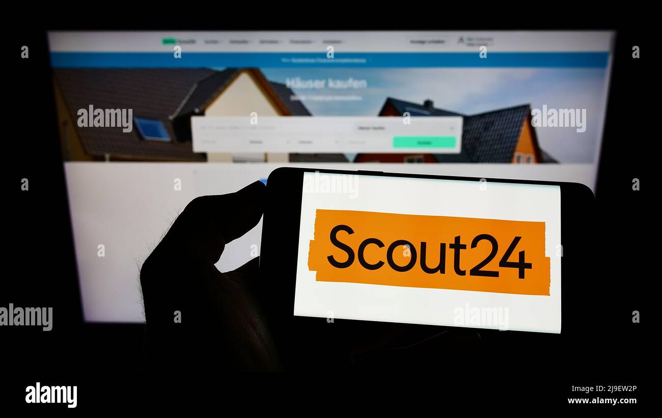 Personne tenant le téléphone portable avec le logo de la société allemande de plateforme immobilière Scout24 se sur l'écran devant la page web. Mise au point sur l'affichage du téléphone. Banque D'Images