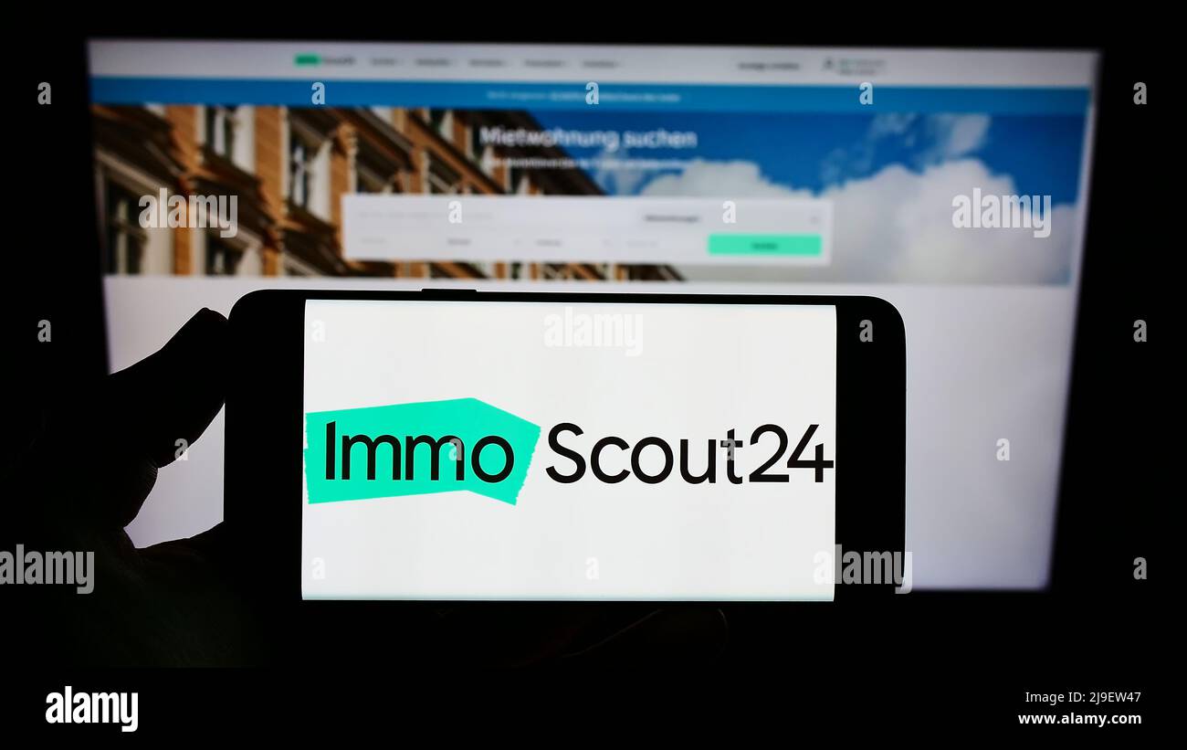 Personne tenant un téléphone portable avec logo de la plate-forme immobilière ImmoScout24 (Scout24 se) à l'écran en face de la page web. Mise au point sur l'affichage du téléphone. Banque D'Images