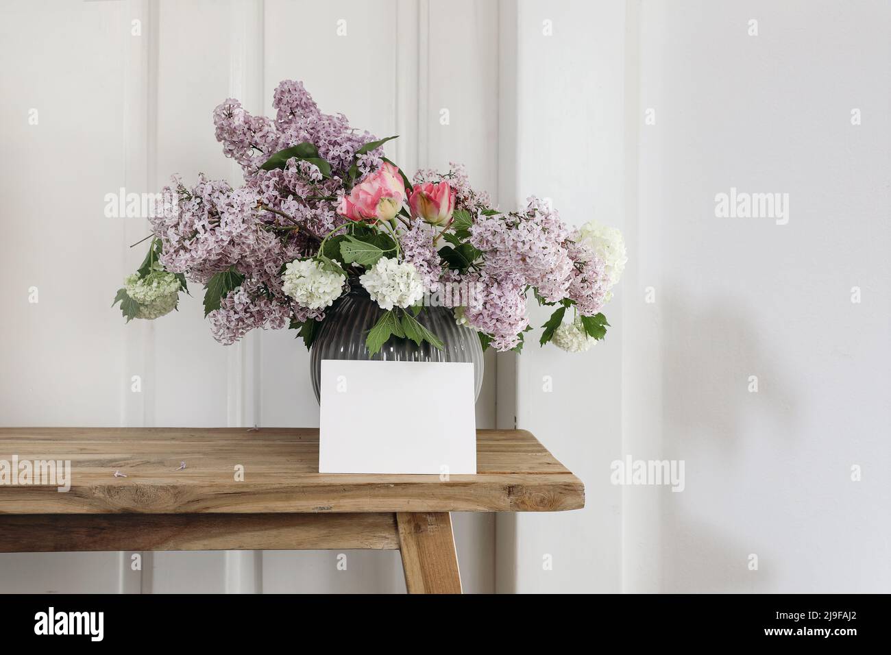 La vie au printemps. Carte de vœux horizontale vierge, invitation. Vase avec bouquet de lilas, viburnum et tulipes sur une ancienne table en bois. Bois blanc Banque D'Images