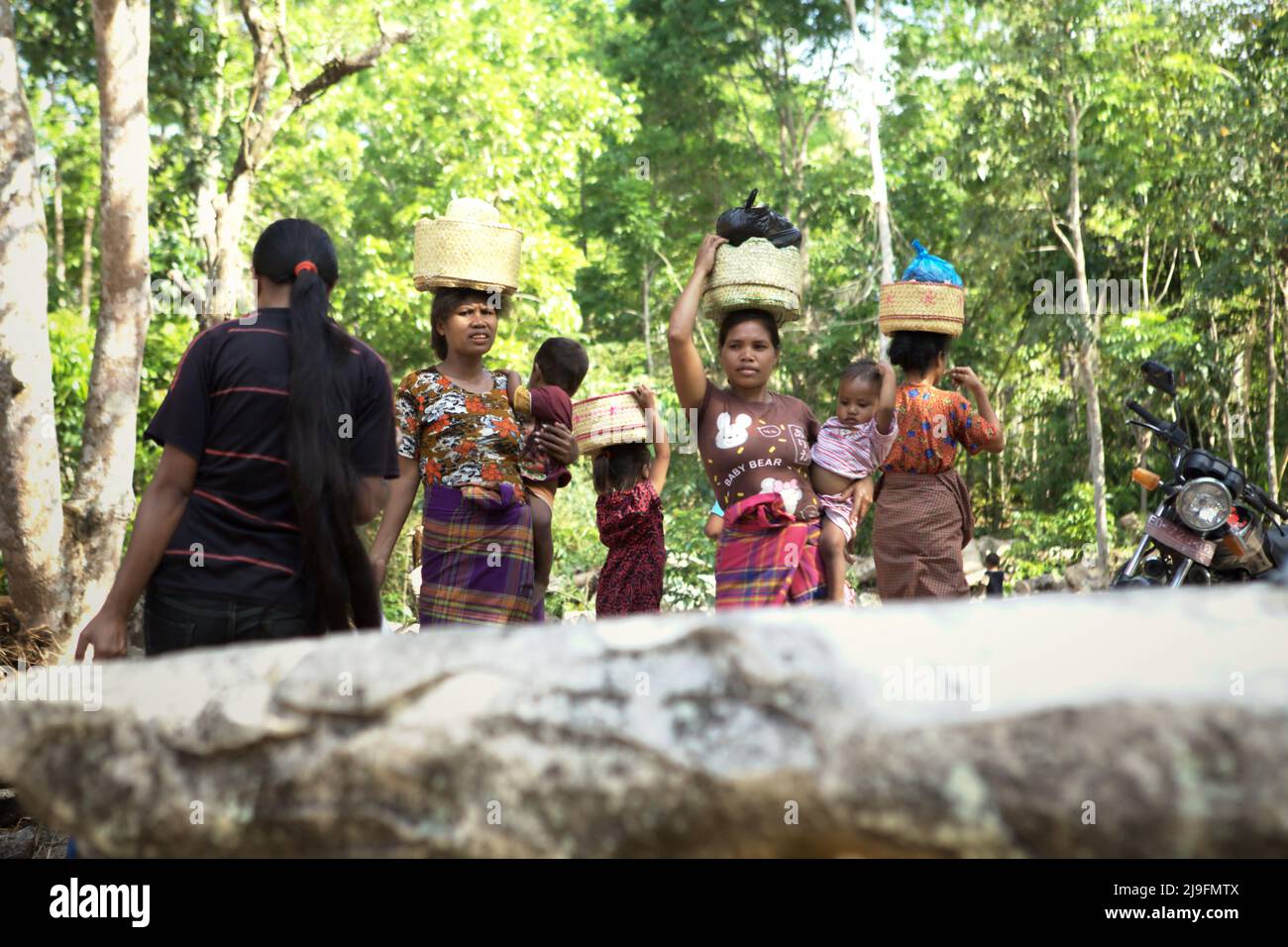 Les femmes transportant des enfants à la main et des aliments sur leur tête lorsqu'elles marchent dans le village traditionnel de Praijing à Tebara, Waikabubak, West Sumba, East Nusa Tenggara, Indonésie. Banque D'Images