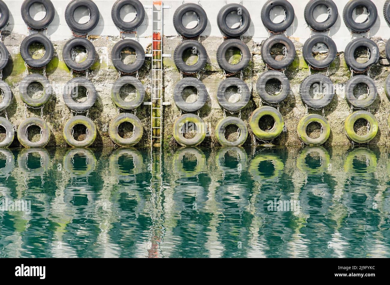 Vieux pneus de voiture pour la gestion de la coque des navires d'amarrage, et une échelle d'urgence attachée à un mur de béton rugueux dans un petit harbou rin Islande Banque D'Images