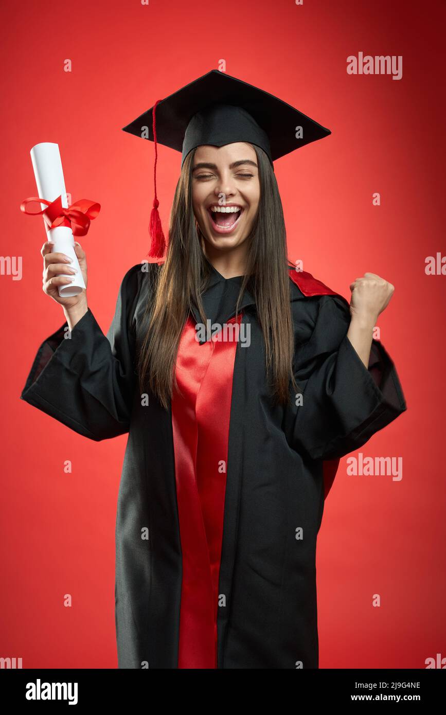 Vue de face d'une fille heureuse et heureuse qui obtient son diplôme d'études collégiales, universitaires, secondaires. Jolie jeune femme debout avec les yeux fermés, tenant le diplôme, riant. Concept d'éducation. Banque D'Images Vue de face d'une fille heureuse et heureuse qui obtient son diplôme d'études collégiales, universitaires, secondaires. Jolie jeune femme debout avec les yeux fermés, tenant le diplôme, riant. Concept d'éducation. Banque D'Images