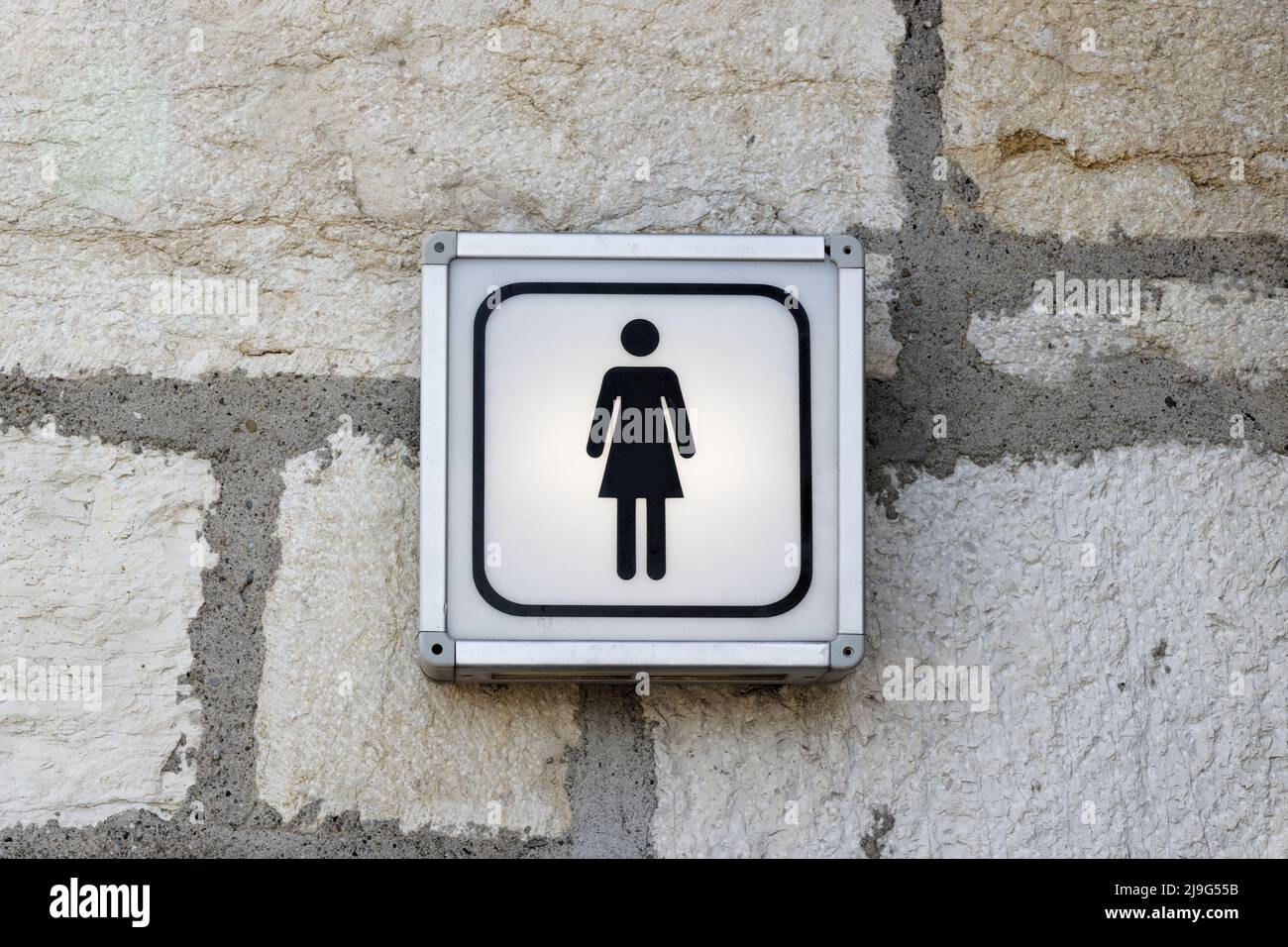 panneau lumineux pour toilettes des femmes fixé sur un mur en pierre blanche, ce qui facilite la recherche d'un endroit calme, sans personne, pendant la journée Banque D'Images