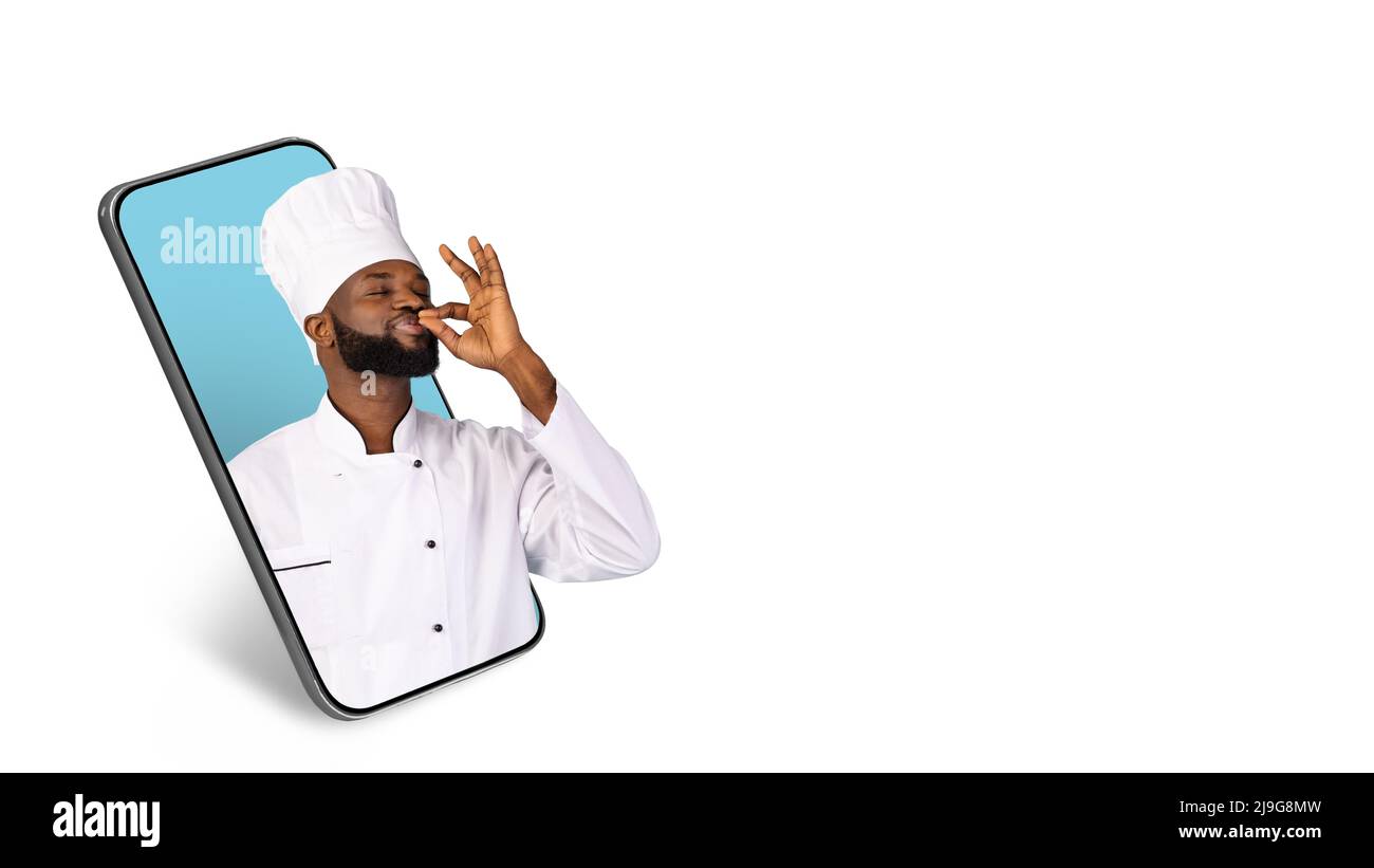Un chef masculin noir se baiser les doigts tout en se faisant sortir de l'écran du grand smartphone Banque D'Images