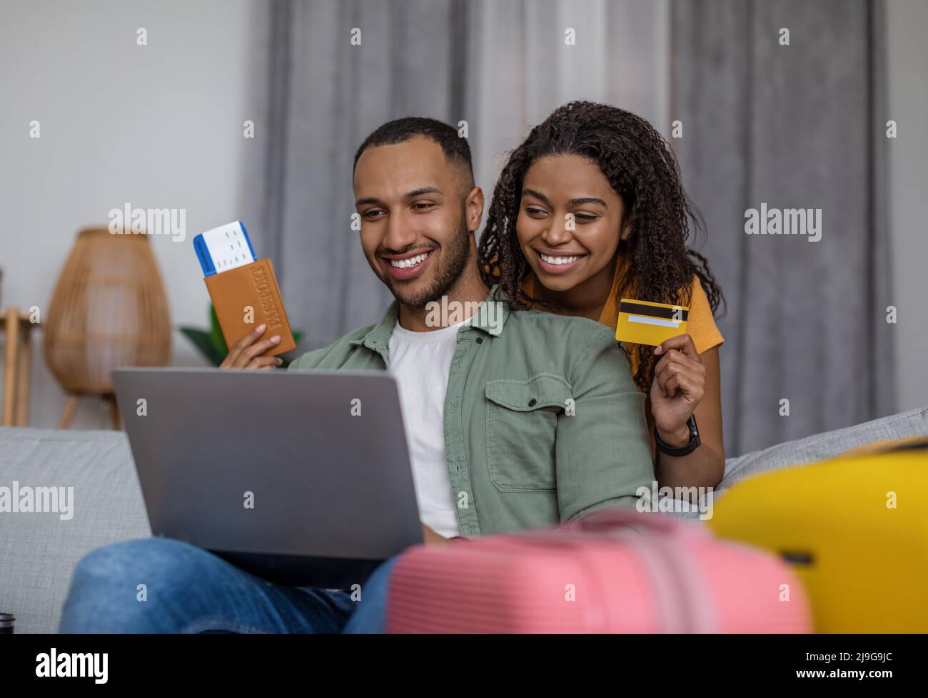 Un heureux couple afro-américain utilisant un ordinateur portable et réserver un hôtel avec une carte de crédit, assis avec des valises, prêt à partir Banque D'Images