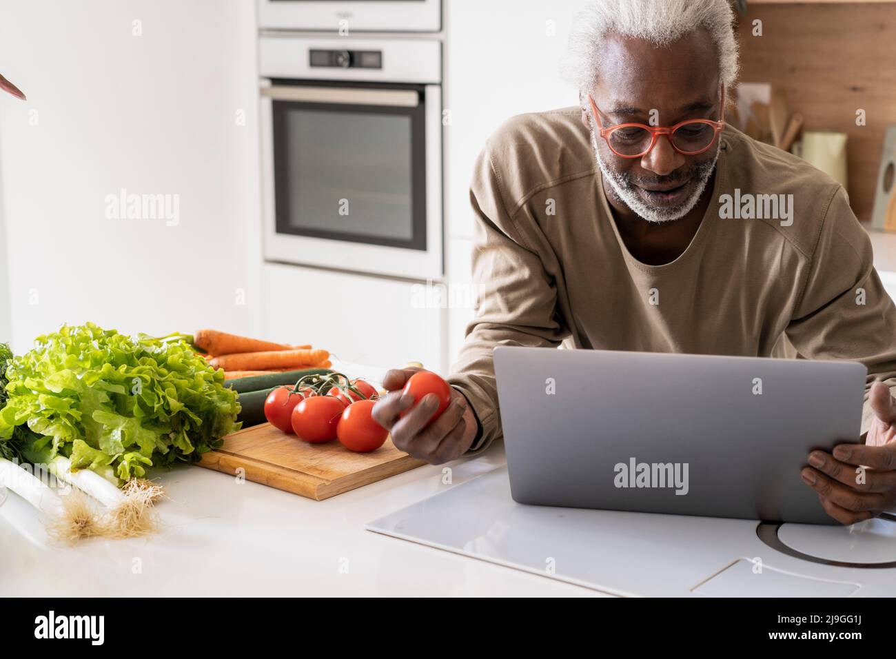 Homme senior regardant un reçu sur un ordinateur portable tout en se penchant sur le plan de travail de la cuisine Banque D'Images