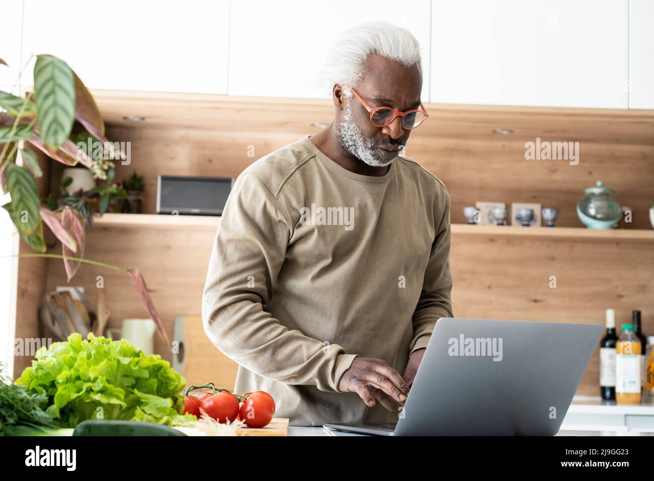 Homme senior regardant la recette sur un ordinateur portable dans la cuisine Banque D'Images