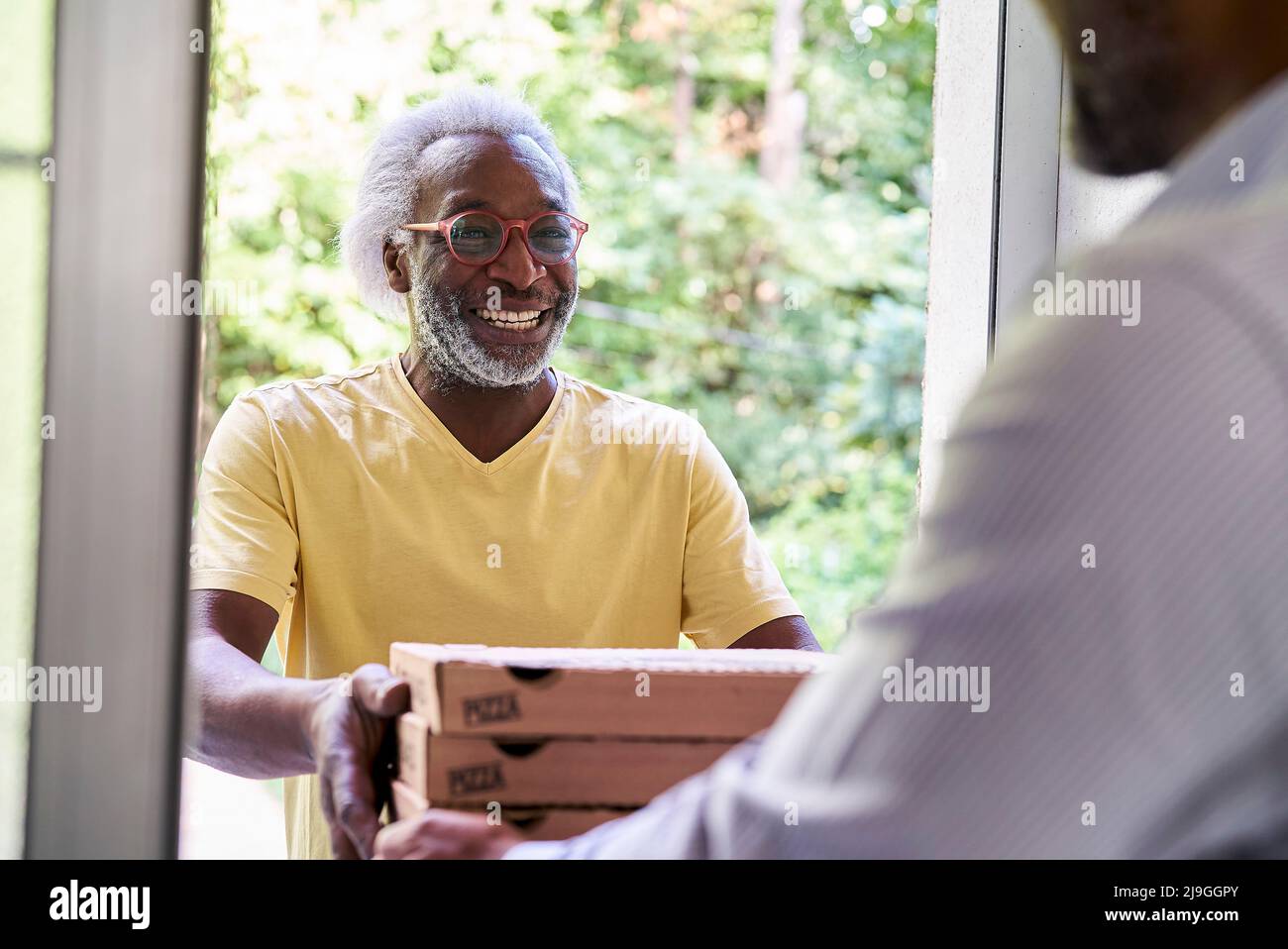 Un livreur senior livrant une pizza à l'homme à la porte Banque D'Images