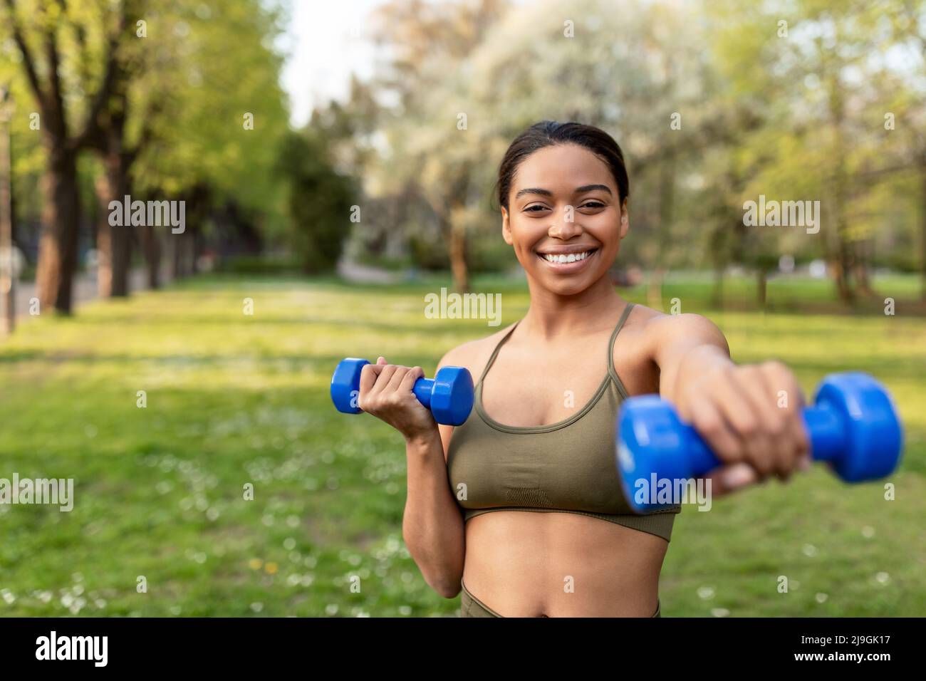 Bonne jeune femme noire faisant l'entraînement de force en plein air, s'exerçant avec des haltères, l'exercice de ses muscles de biceps Banque D'Images